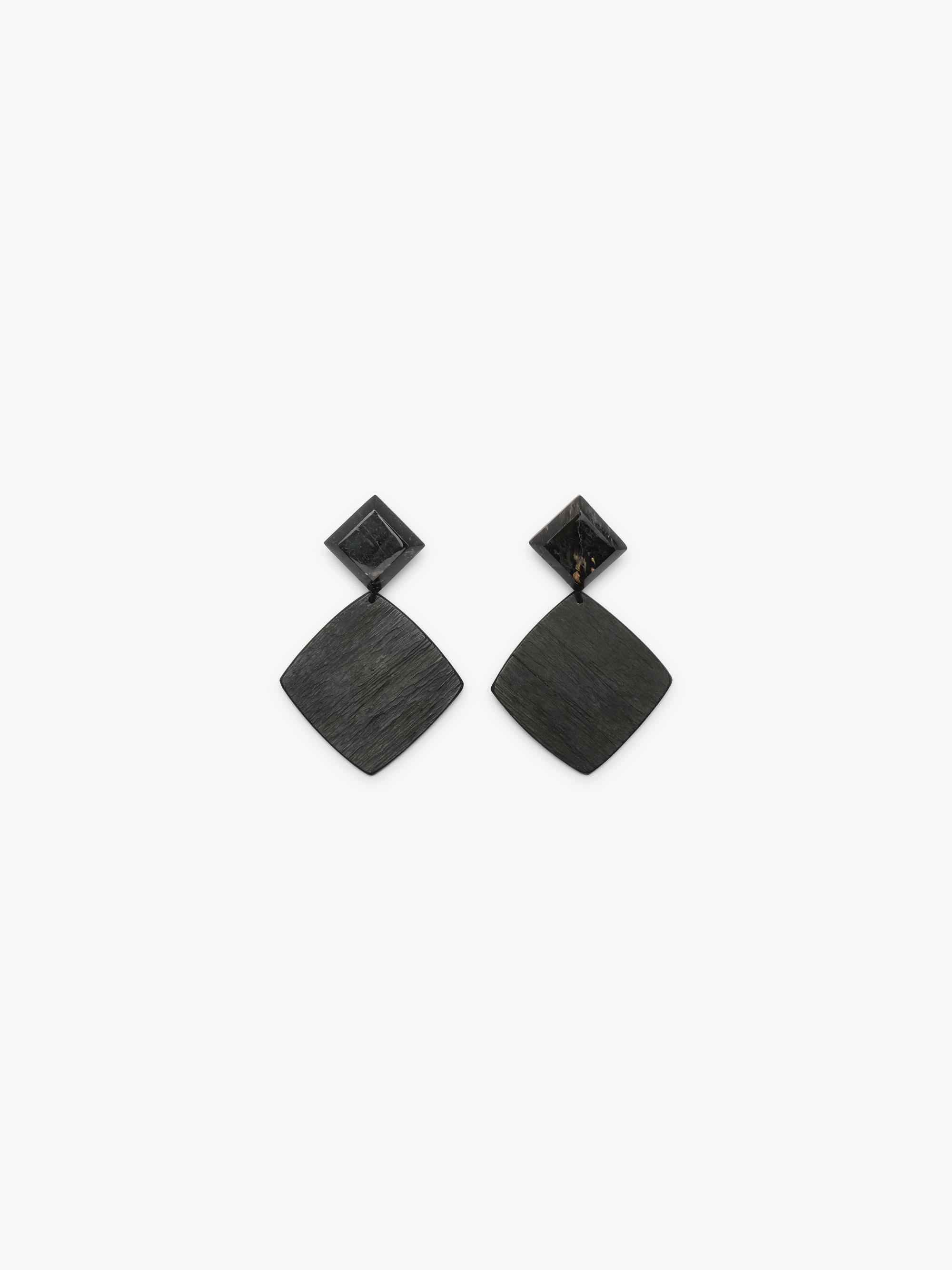 A diamond shaped pair of earrings featuring a black faceted small top and a larger ebony bottom, displayed on a white background