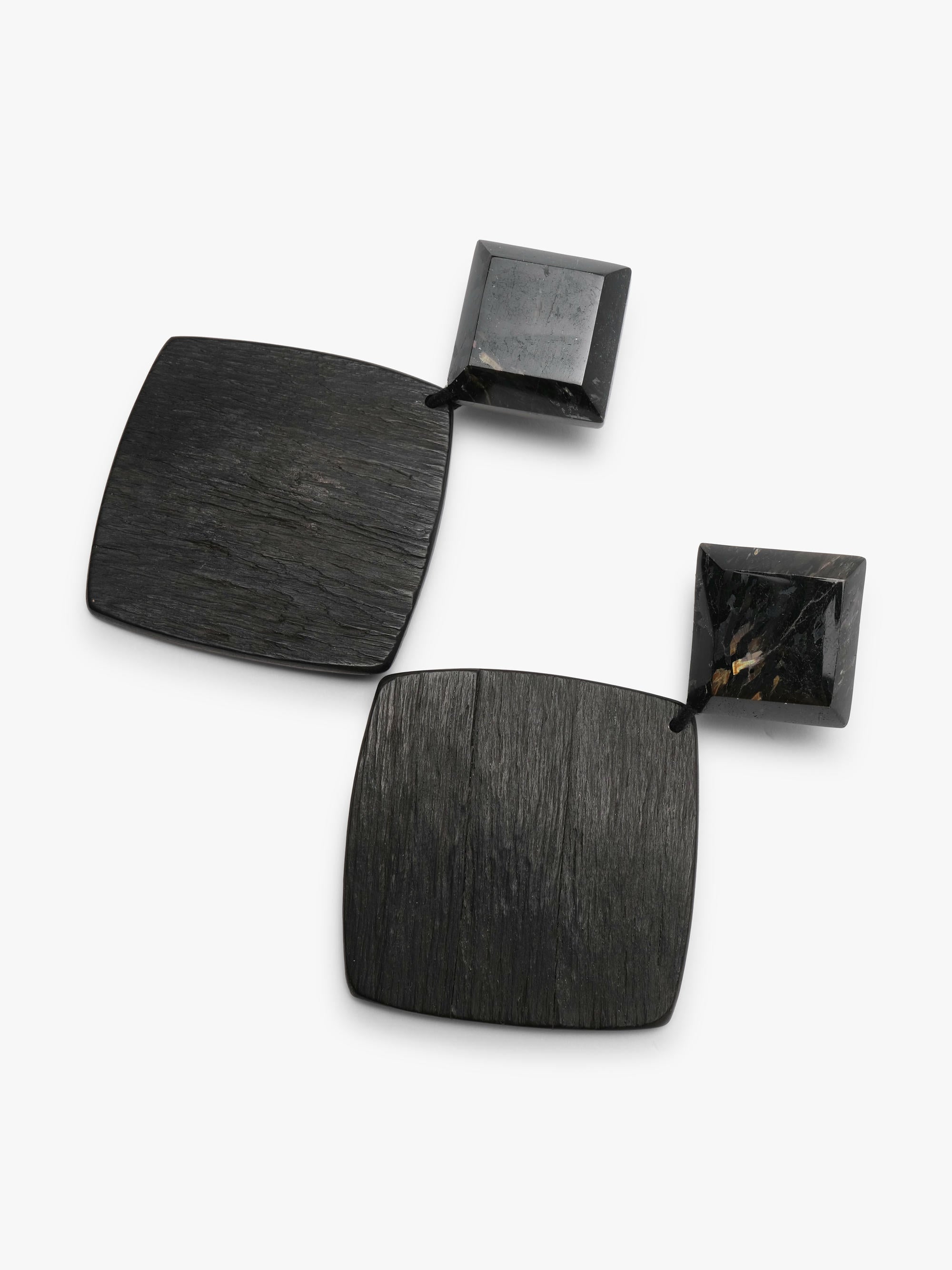 A diamond shaped pair of earrings featuring a black faceted small top and a larger ebony bottom, displayed on a white background