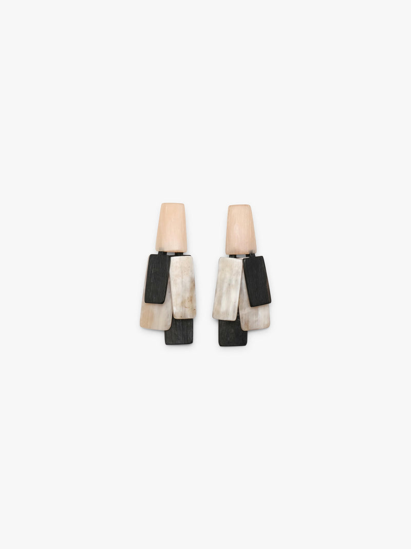 A pair of geometric drop earrings featuring layered rectangular pieces in black, cream, and light peach in horn and wood, set against a plain white background.