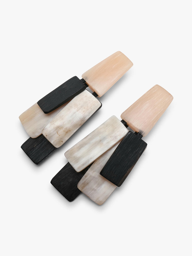 A pair of geometric drop earrings featuring layered rectangular pieces in black, cream, and light peach in horn and wood, set against a plain white background.
