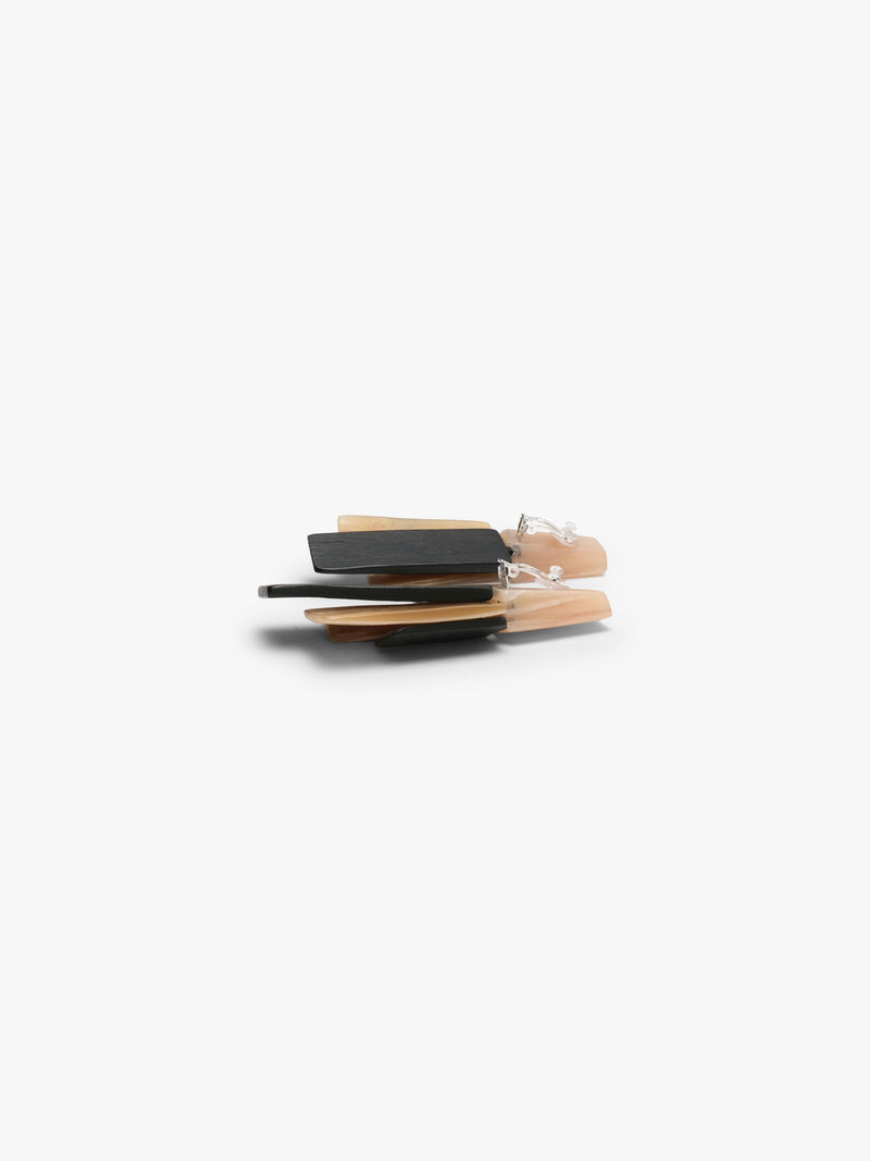 A pair of geometric drop earrings featuring layered rectangular pieces in black, cream, and light peach in horn and wood, set against a plain white background.