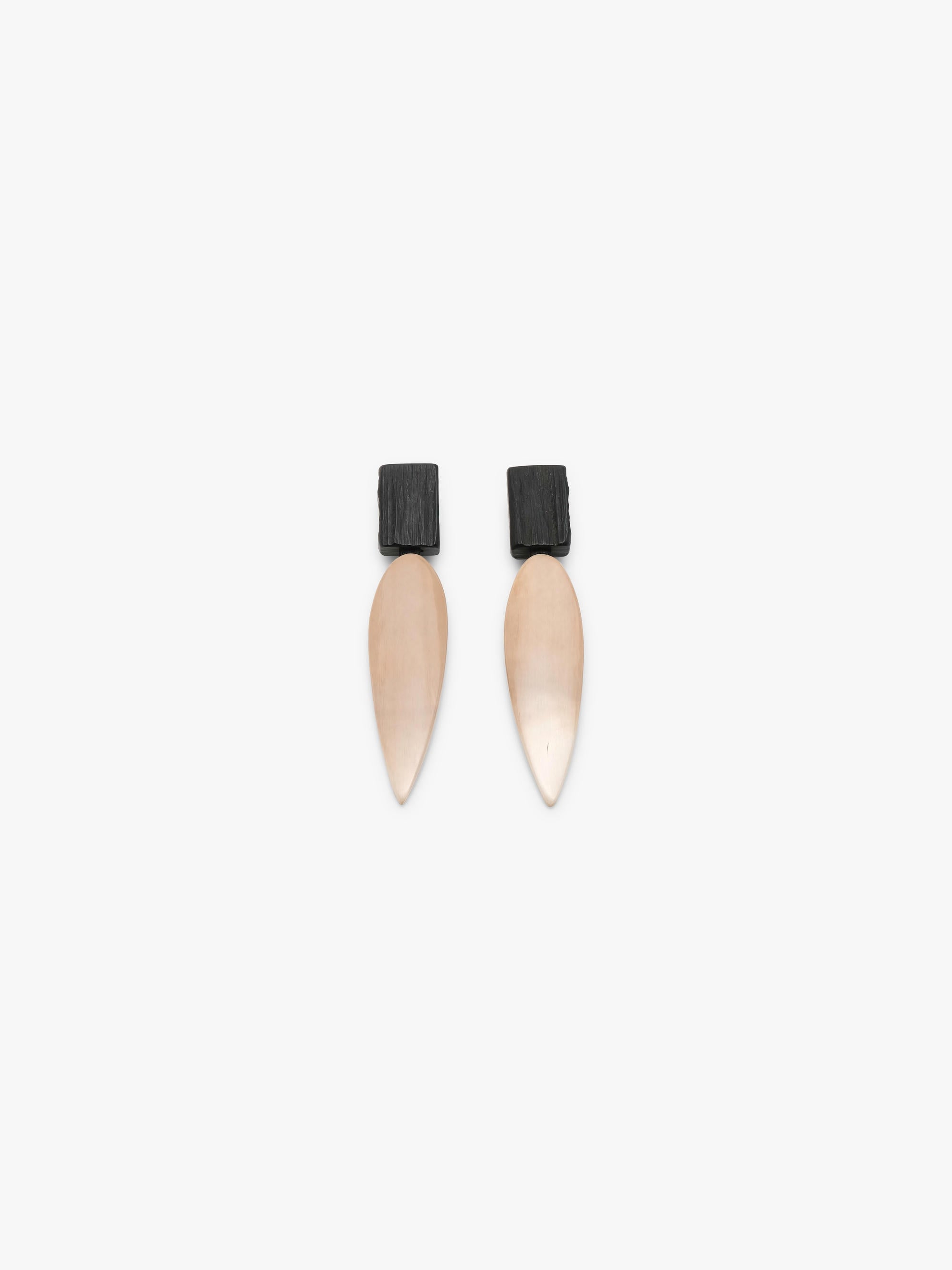 A pair of minimalist drop earrings featuring a matte black rectangular top and a teardrop-shaped pendant in a warm champagne beige finish, set against a solid off-white background.
