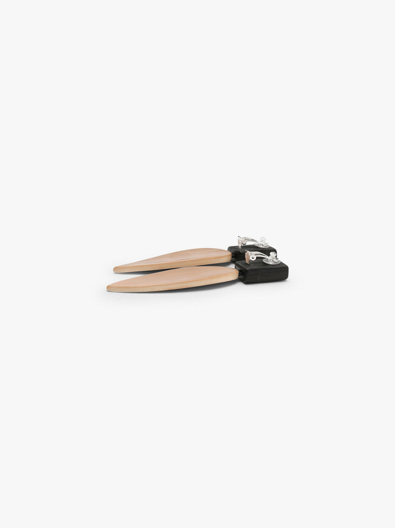 A pair of minimalist drop earrings featuring a matte black rectangular top and a teardrop-shaped pendant in a warm champagne beige finish, set against a solid off-white background.