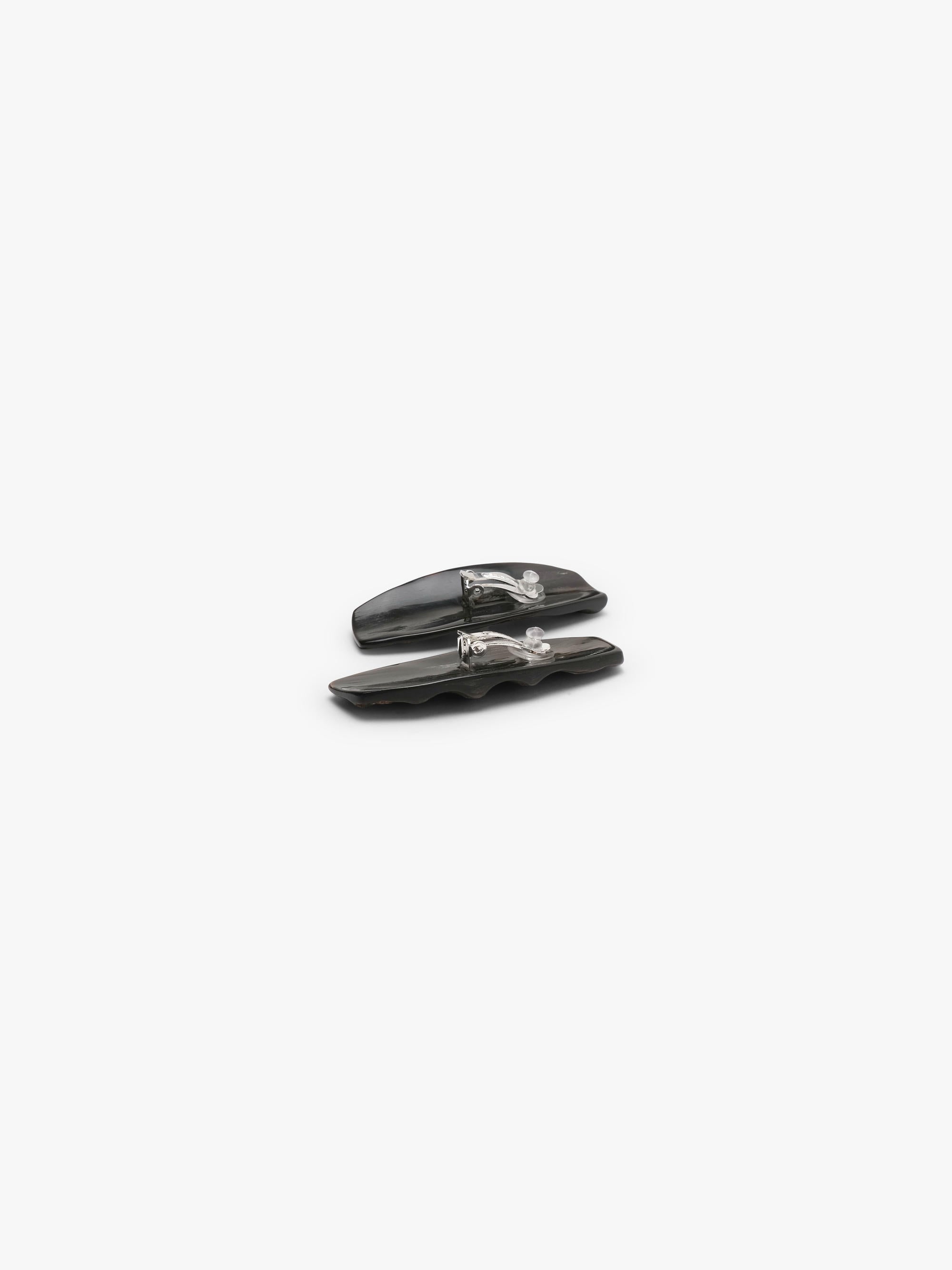 A pair of elongated, textured horn earrings in dark brown, displayed on a white background