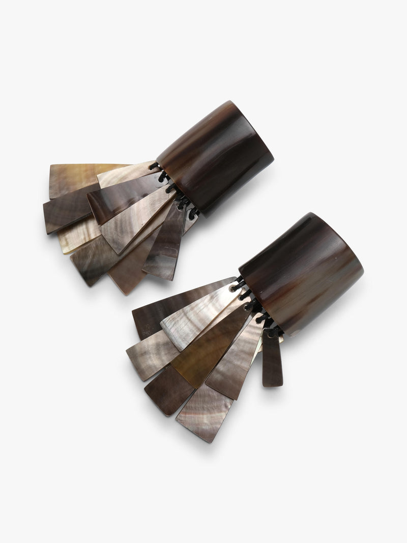 A pair of statement earrings featuring dark brown wooden tops and cascading fan-shaped pearl segments in silver, bronze, and gold tones, set against a plain light gray background.