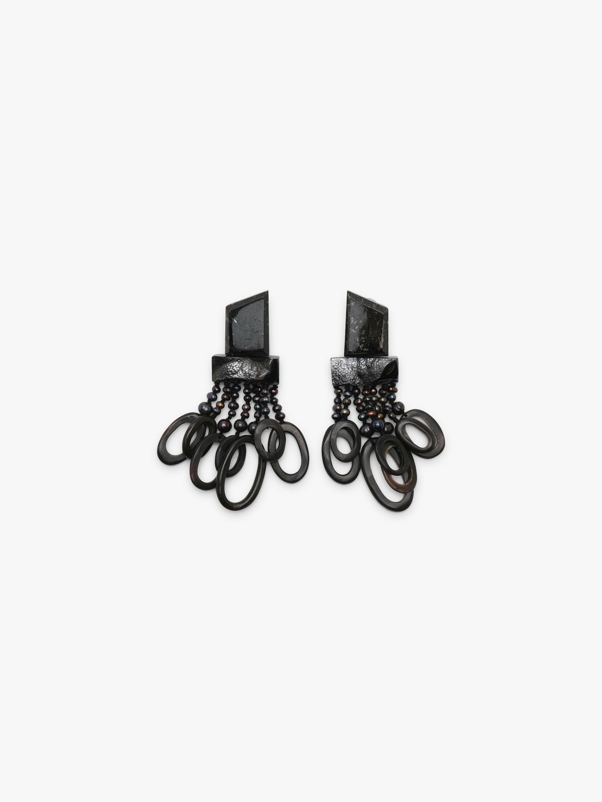 A pair of dramatic black statement earrings featuring textured geometric metal tops, dark beads, and layered black circular rings, displayed on a clean white background.