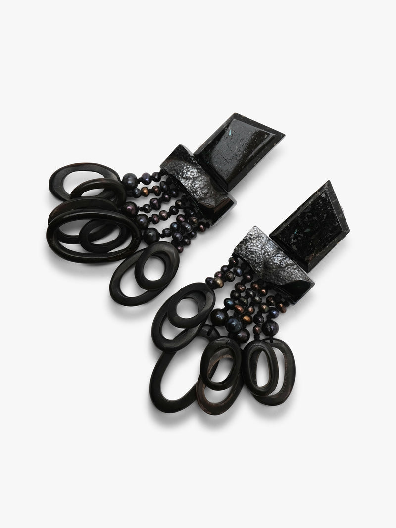 A pair of dramatic black statement earrings featuring textured geometric metal tops, dark beads, and layered black circular rings, displayed on a clean white background.