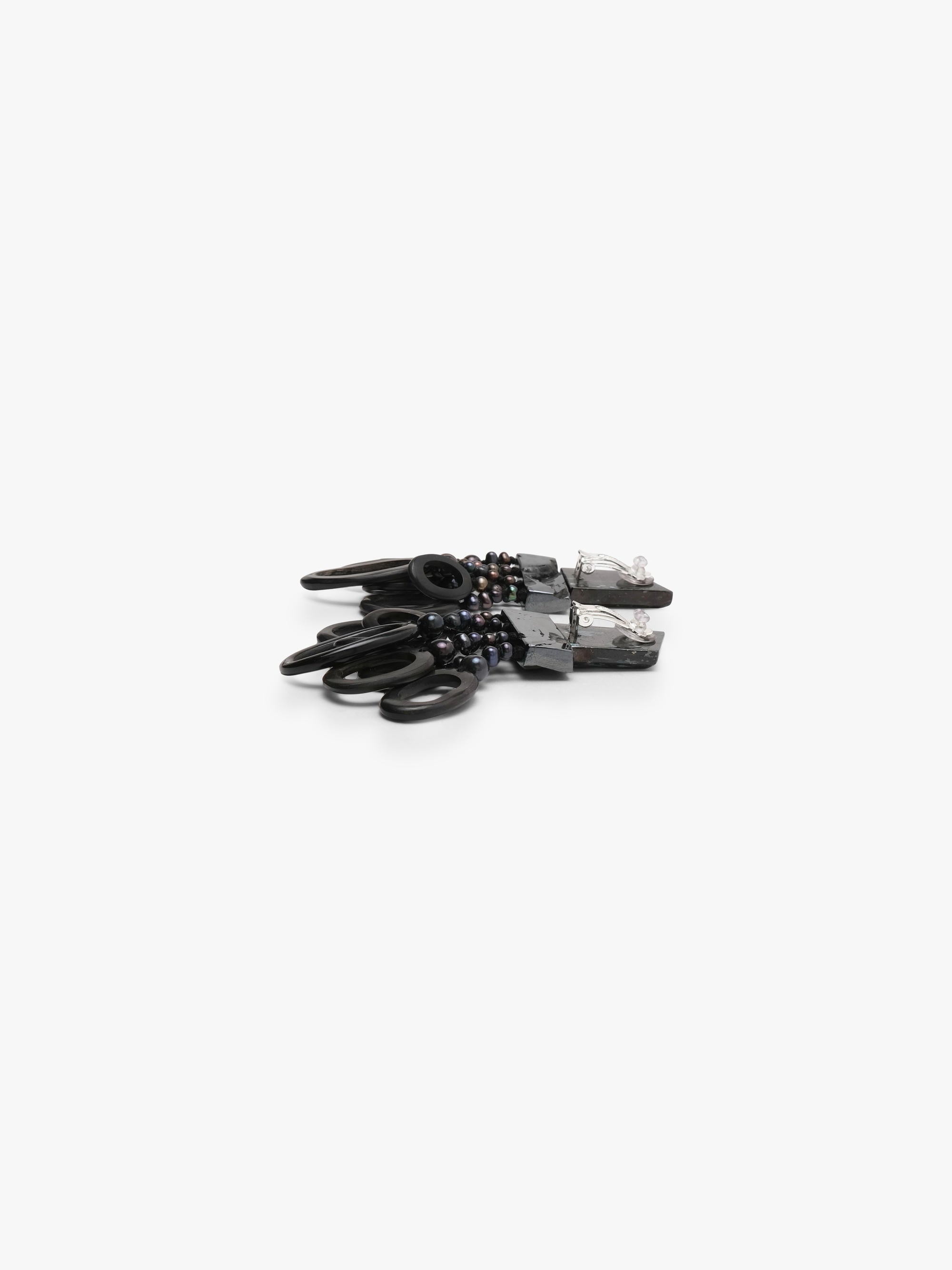 A pair of dramatic black statement earrings featuring textured geometric metal tops, dark beads, and layered black circular rings, displayed on a clean white background.