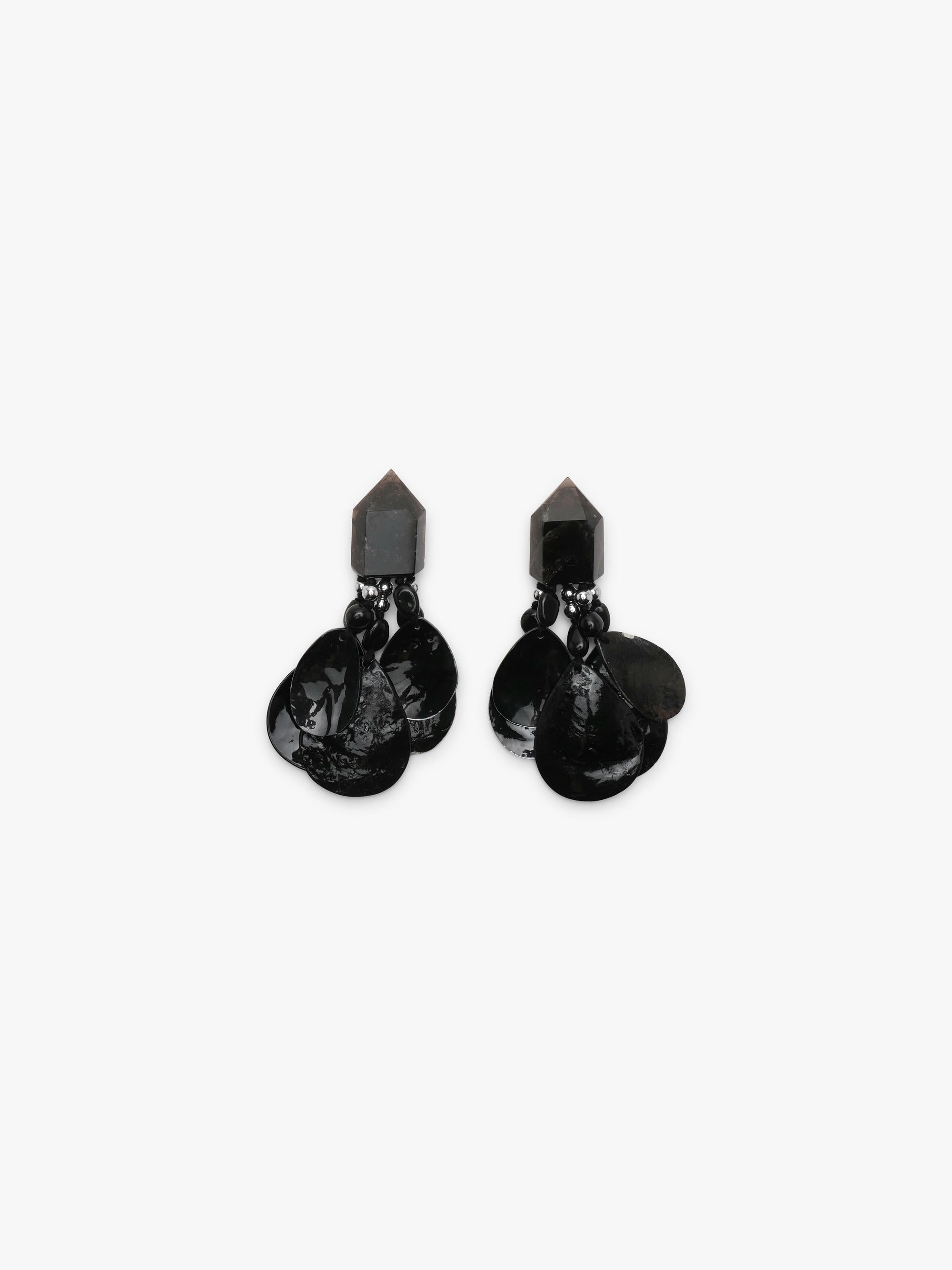 A pair of black dangle earrings with a geometrical top and black shell tassles, displayed on a white background