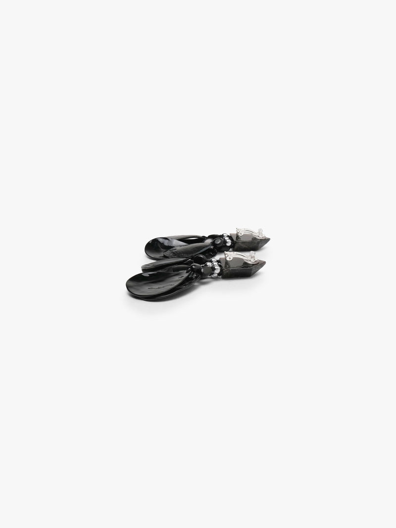A pair of black dangle earrings with a geometrical top and black shell tassles, displayed on a white background