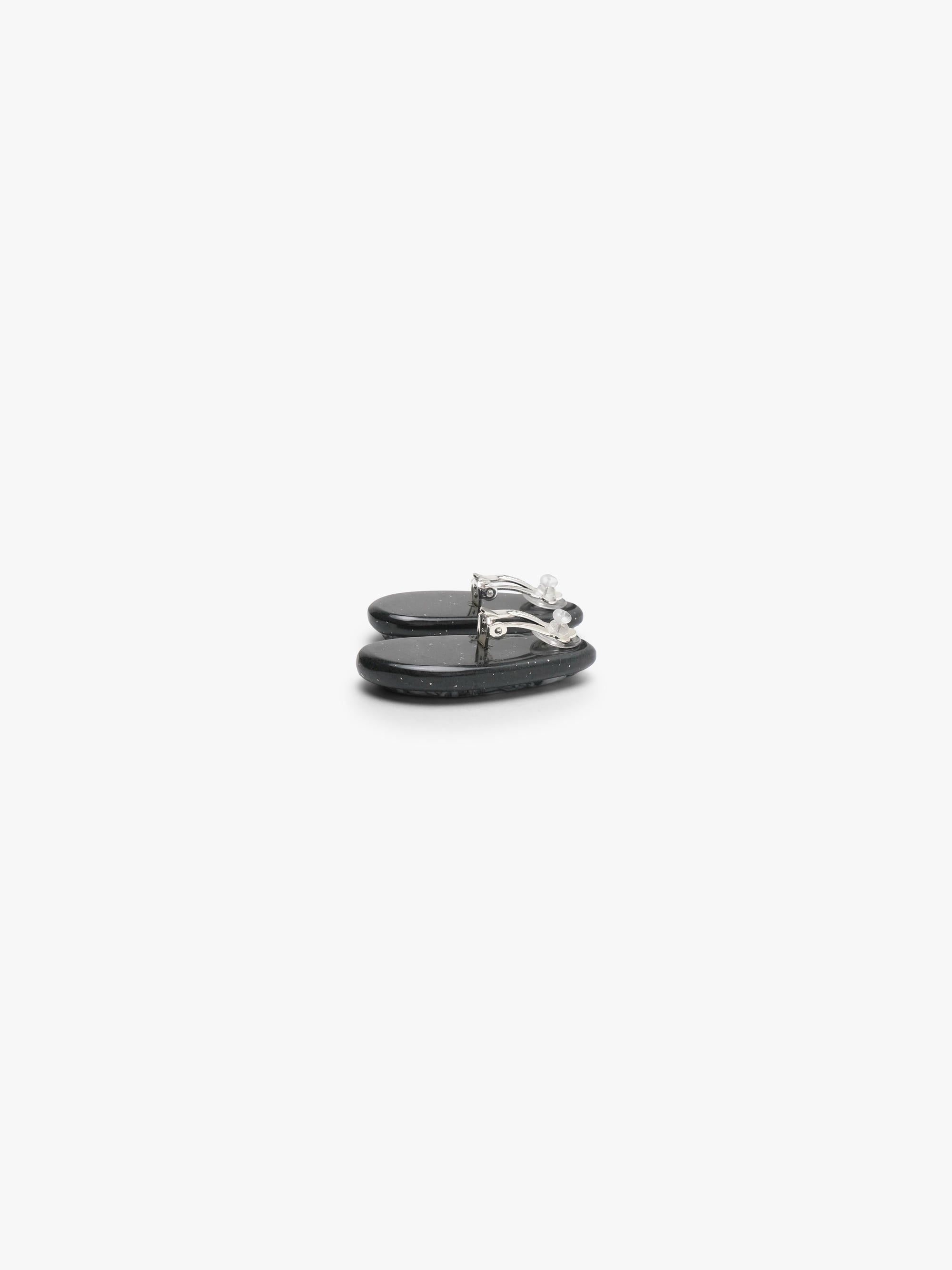 The backside of A pair of black-framed oval stud earrings with white and gray marbled stone inlays, displayed on a clean white background.