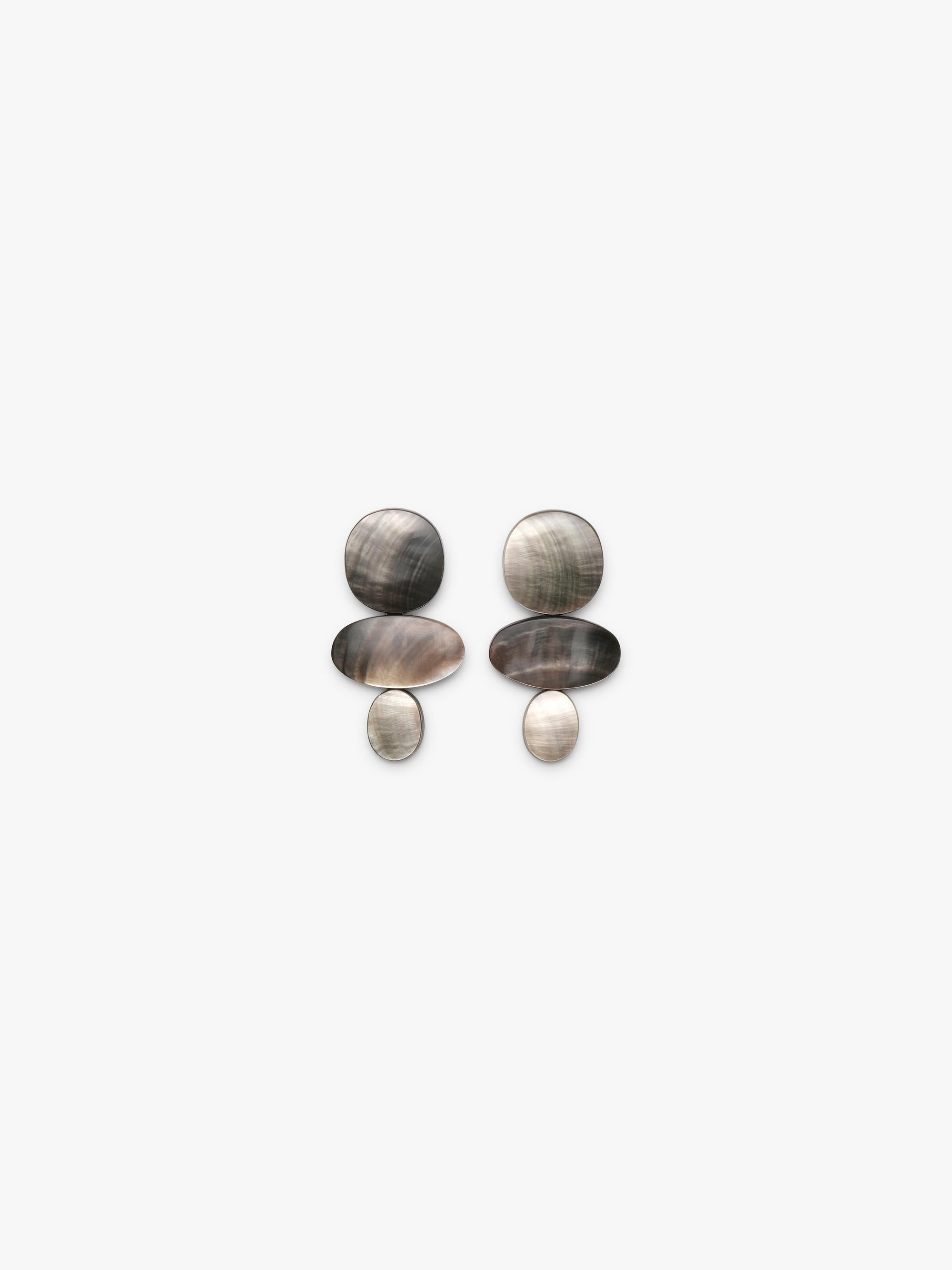 A pair of bohemian-style earrings featuring oval and circular shell-like pieces in natural gray, brown, and beige tones, displayed against a solid off-white background.