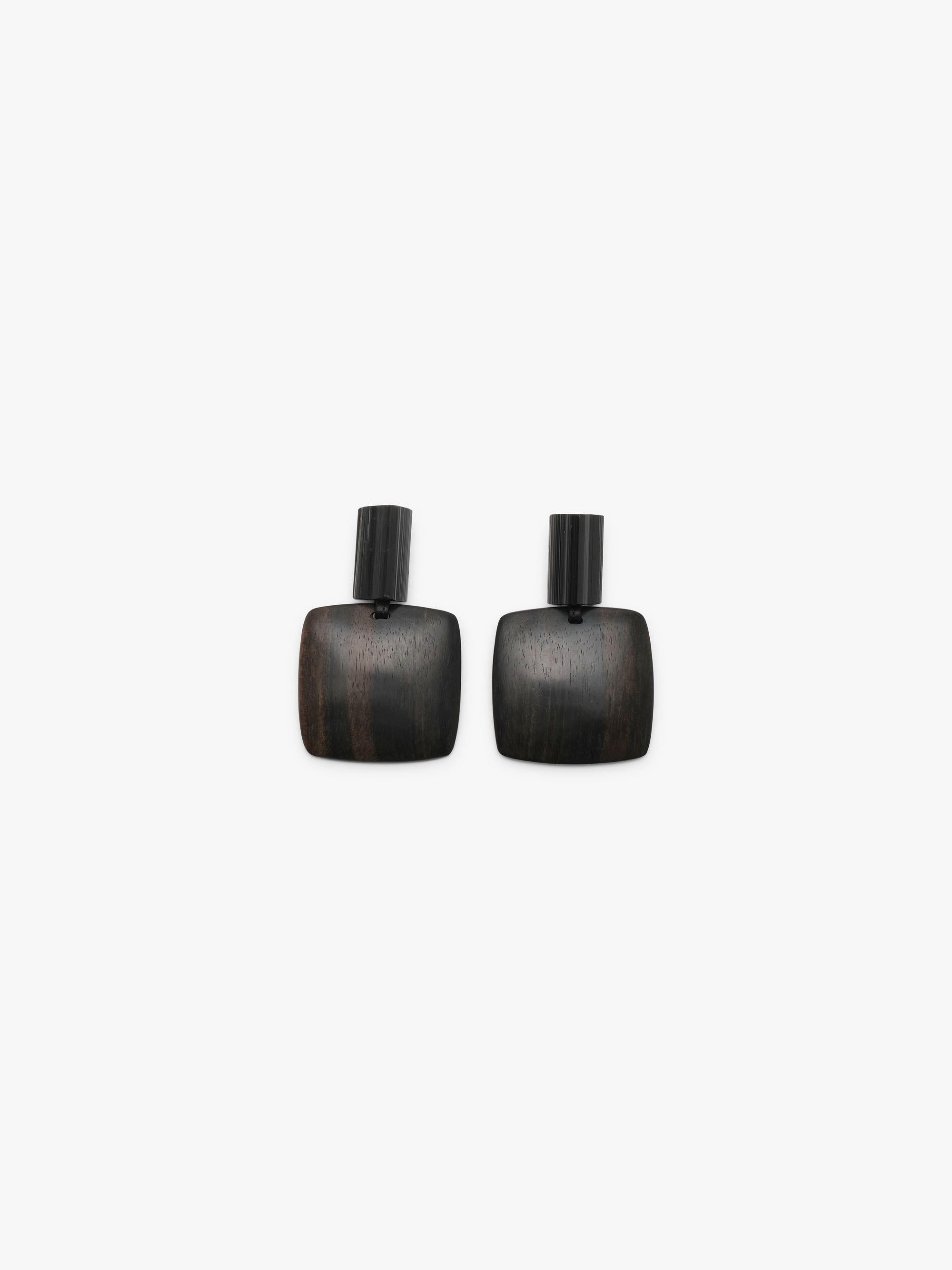 A pair of earrings with small textured black tops and a larger wooden disk underneath, on a white background