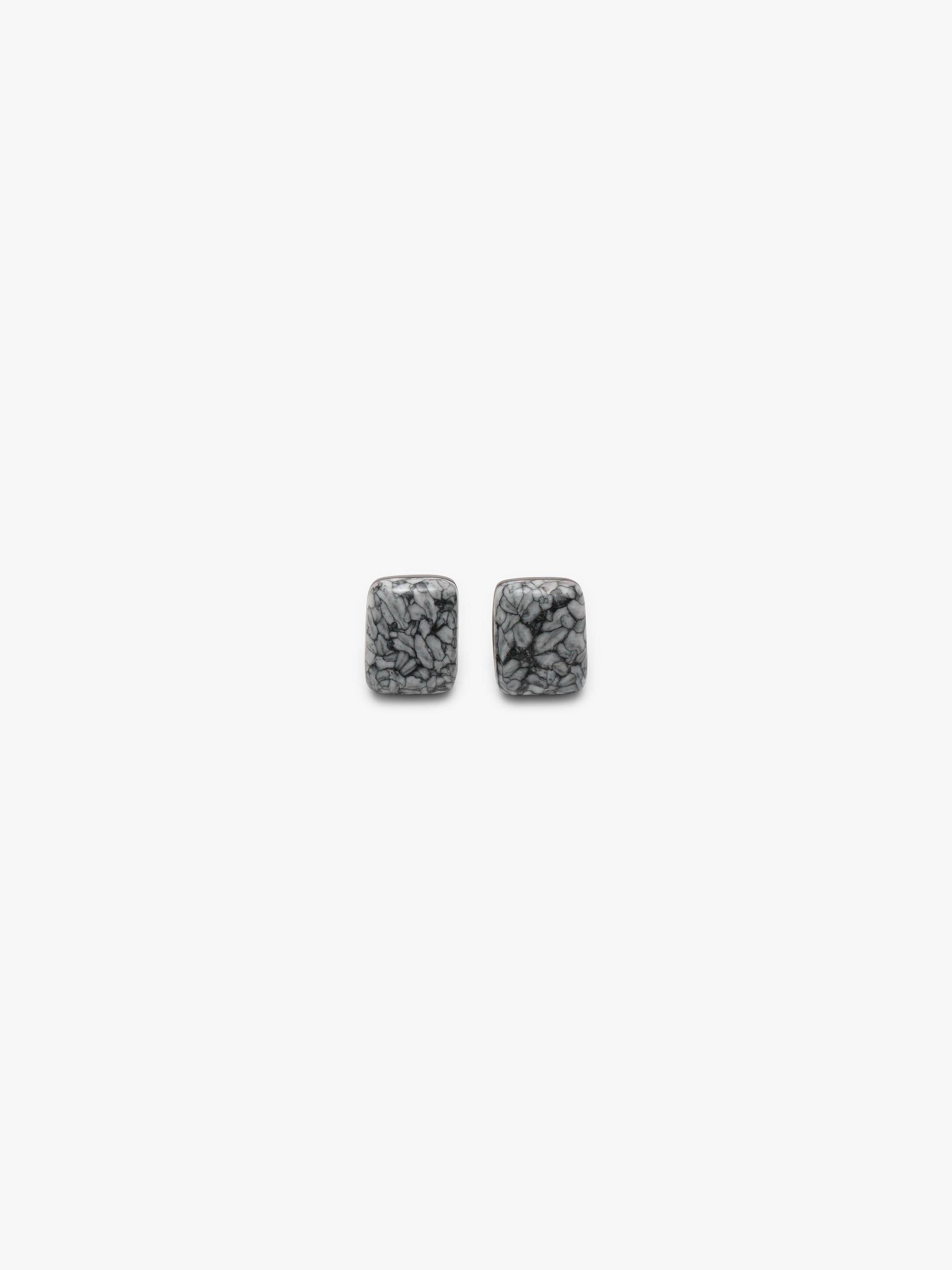 A pair of small rectangular stud earrings with a textured, marbled gray and black pattern, shown against a solid off-white background.