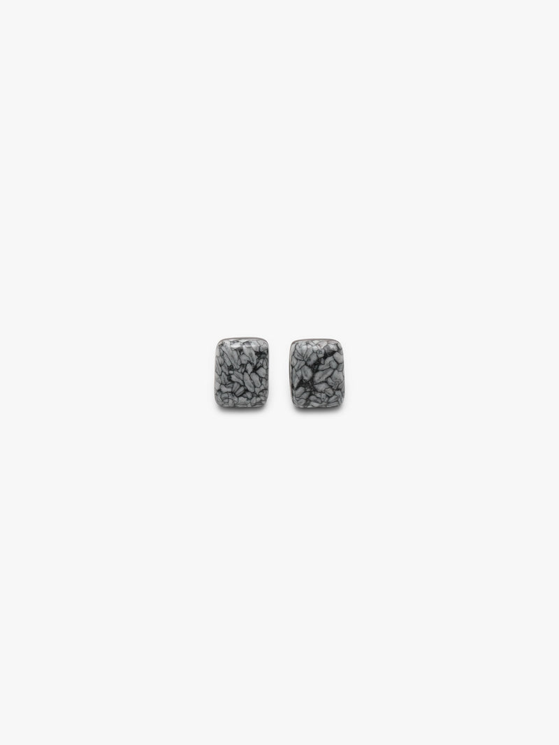 A pair of small rectangular stud earrings with a textured, marbled gray and black pattern, shown against a solid off-white background.