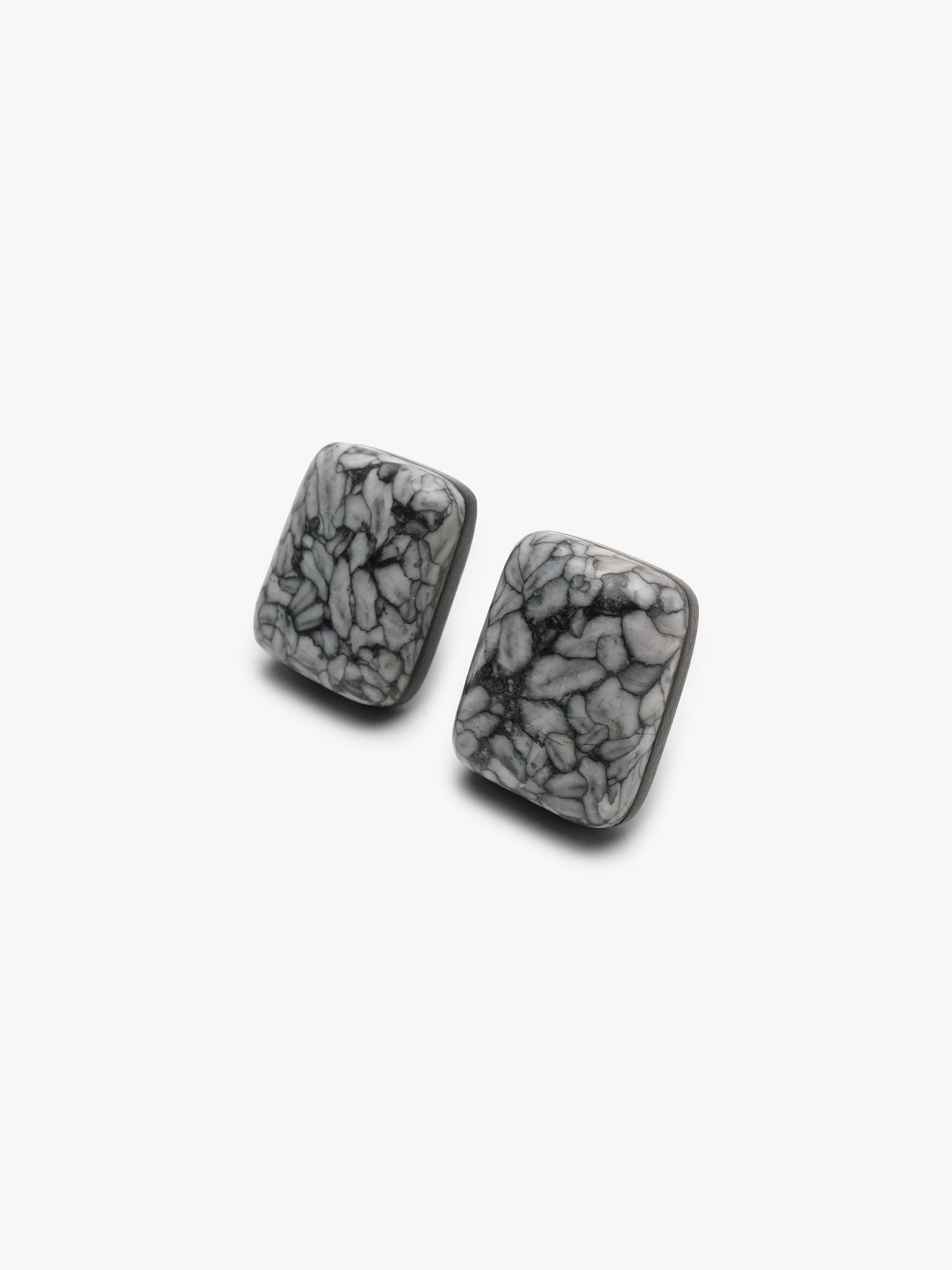 A pair of button earrings with a black and grey marble pattern, displayed on a white background