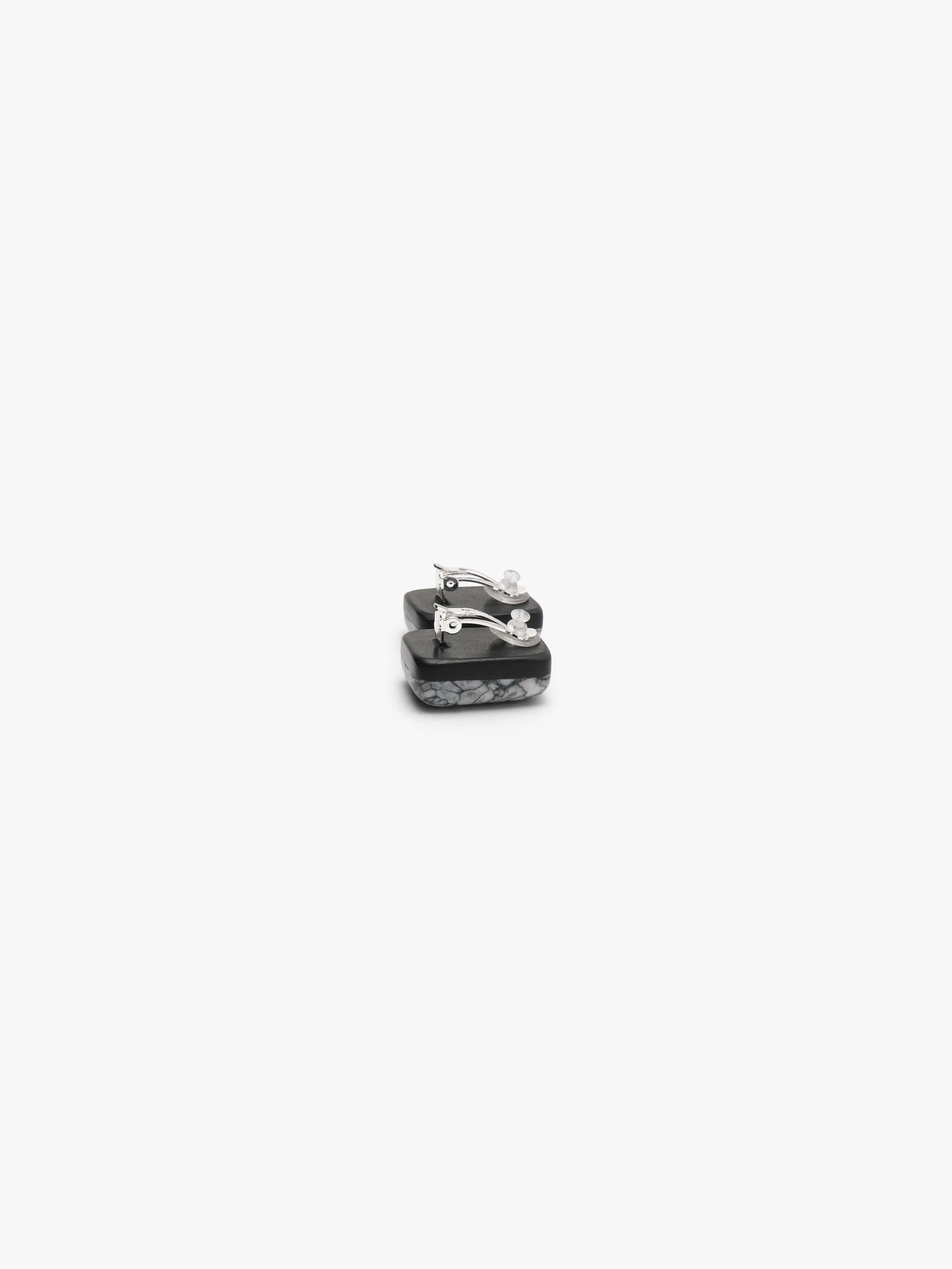 The backside of A pair of small rectangular stud earrings with a textured, marbled gray and black pattern, shown against a solid off-white background.