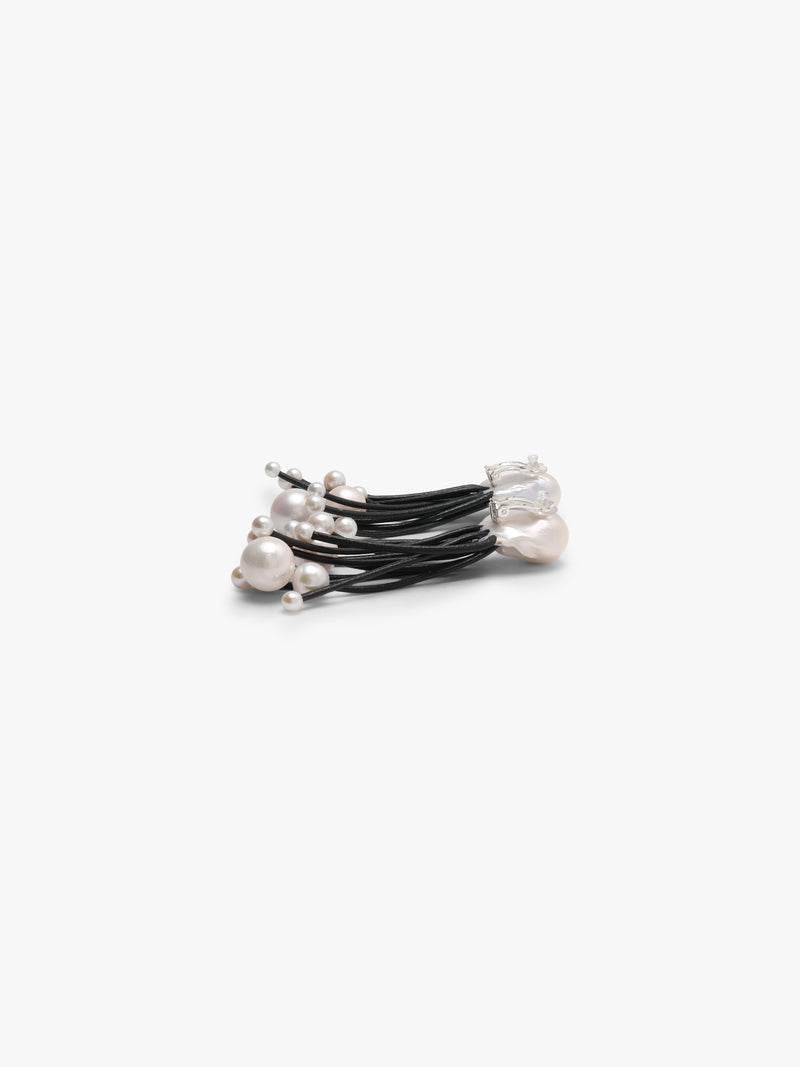 A pair of statement earrings featuring large, irregular white baroque pearls at the top, with multiple thin black cords hanging below, each ending in small white pearl beads, set against a plain light gray background.
