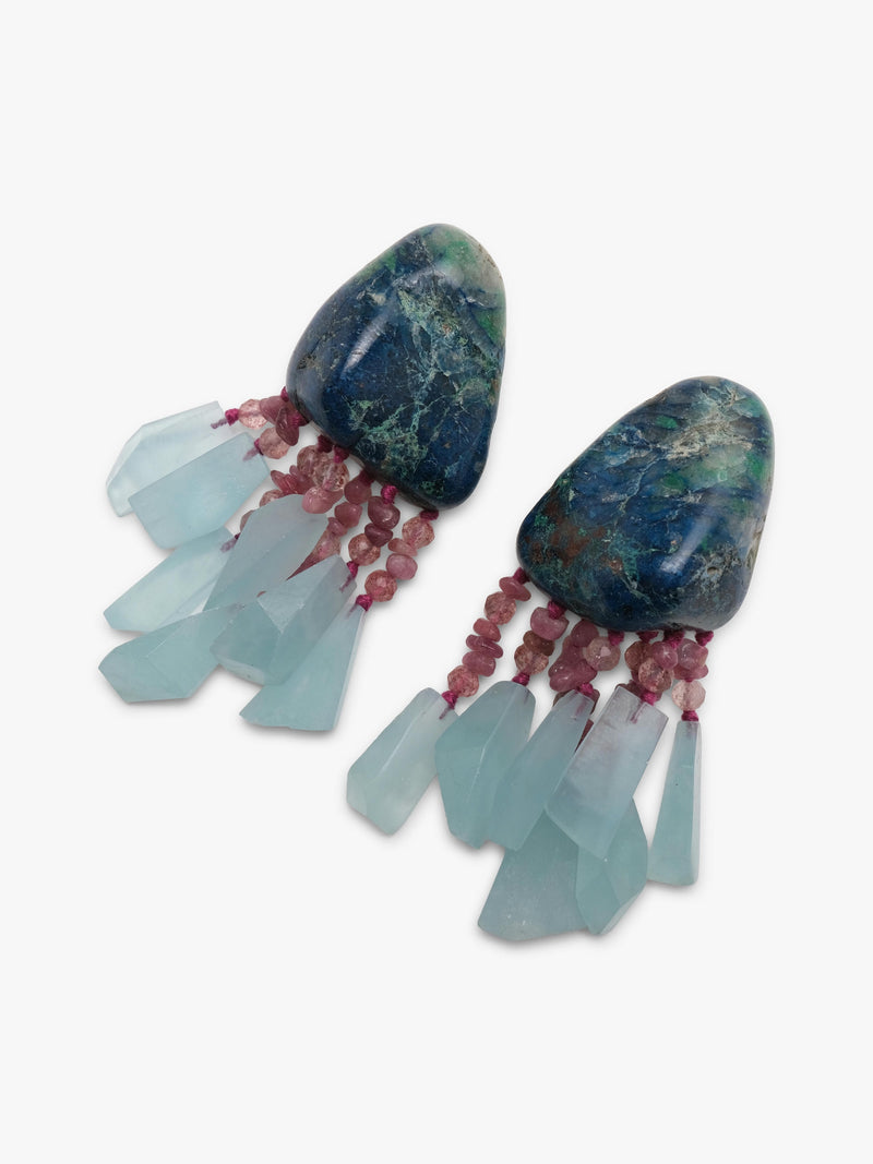 A pair of unique dangle earrings featuring dark blue-green stone tops with delicate pinkish-red fringed details and light blue translucent hanging elements, set against a plain white background.