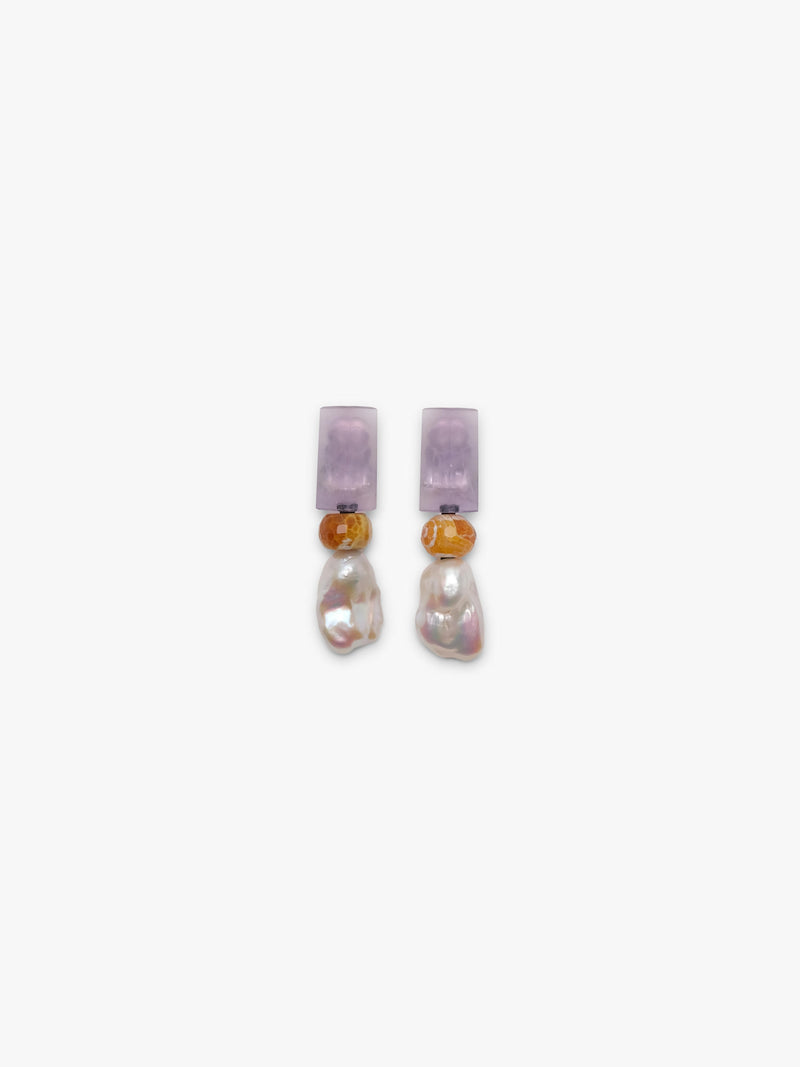 A pair of dangle earrings featuring a lavender rectangular stone, a small amber-brown bead, and a baroque pearl drop, shown on a plain light gray background.