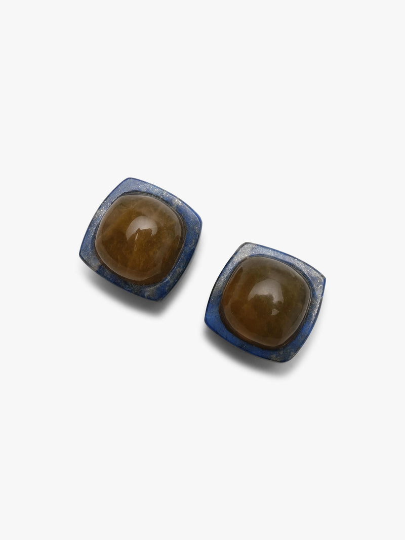 Earrings featuring rounded domeshaped yellow brownish stone set into a deep blue stone. Displayed on a white background. 