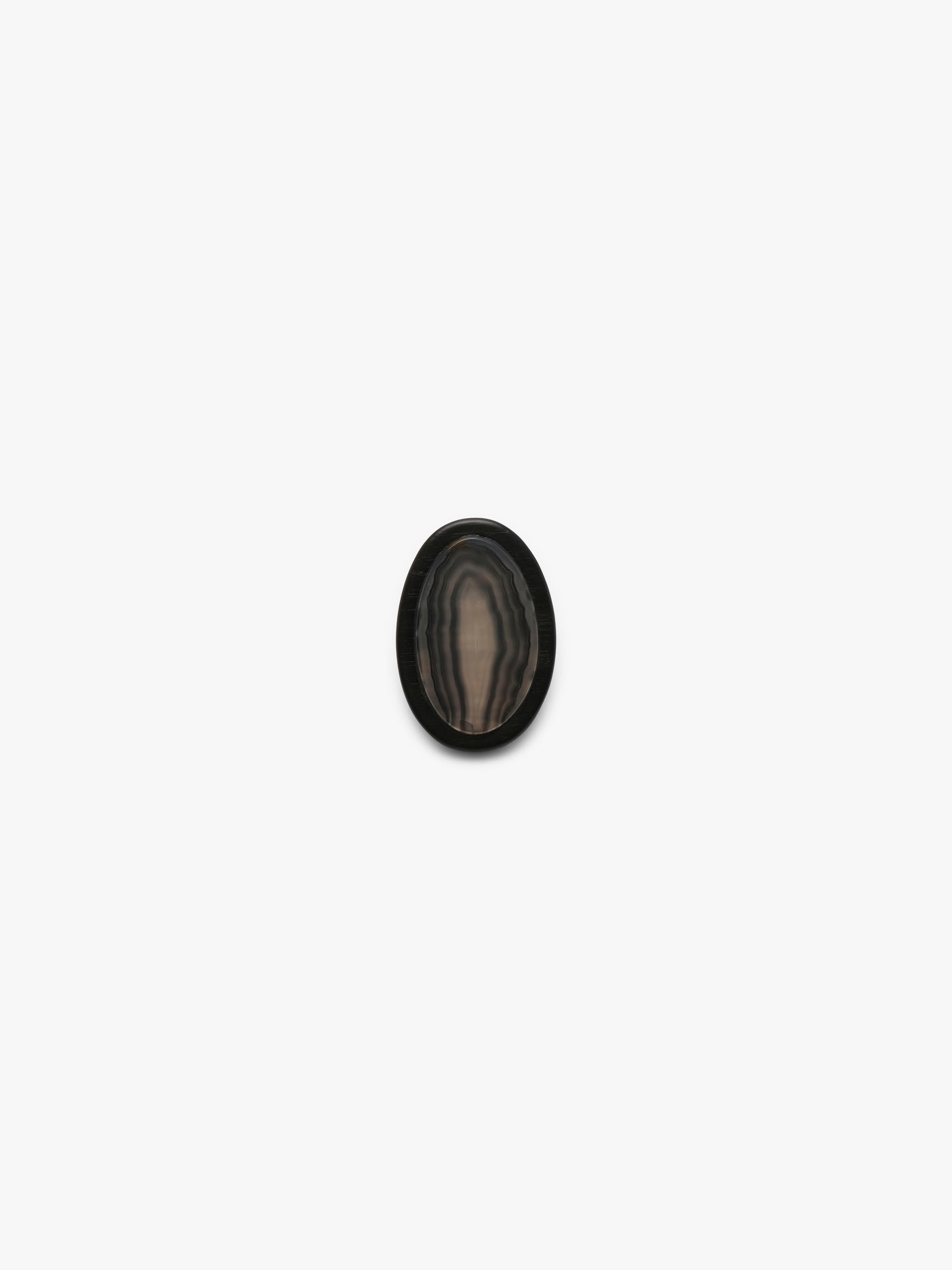 A ring with a patterened black and brown stone , shown against a solid off-white background.