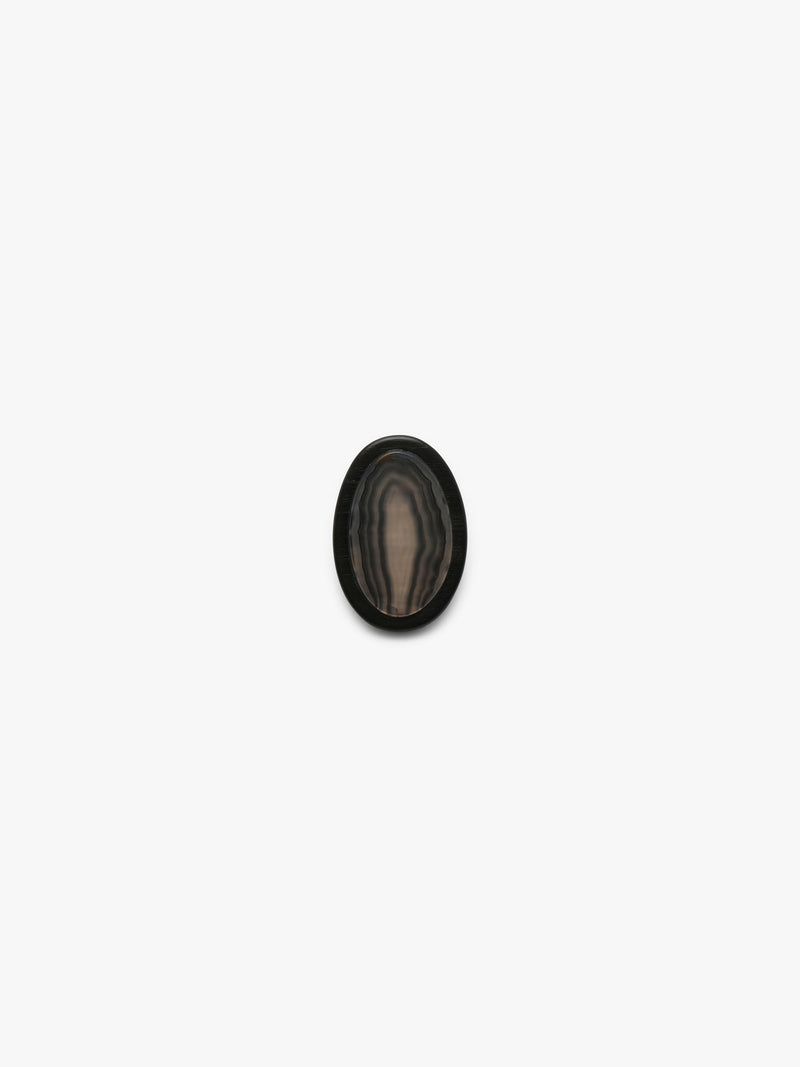A ring with a patterened black and brown stone , shown against a solid off-white background.