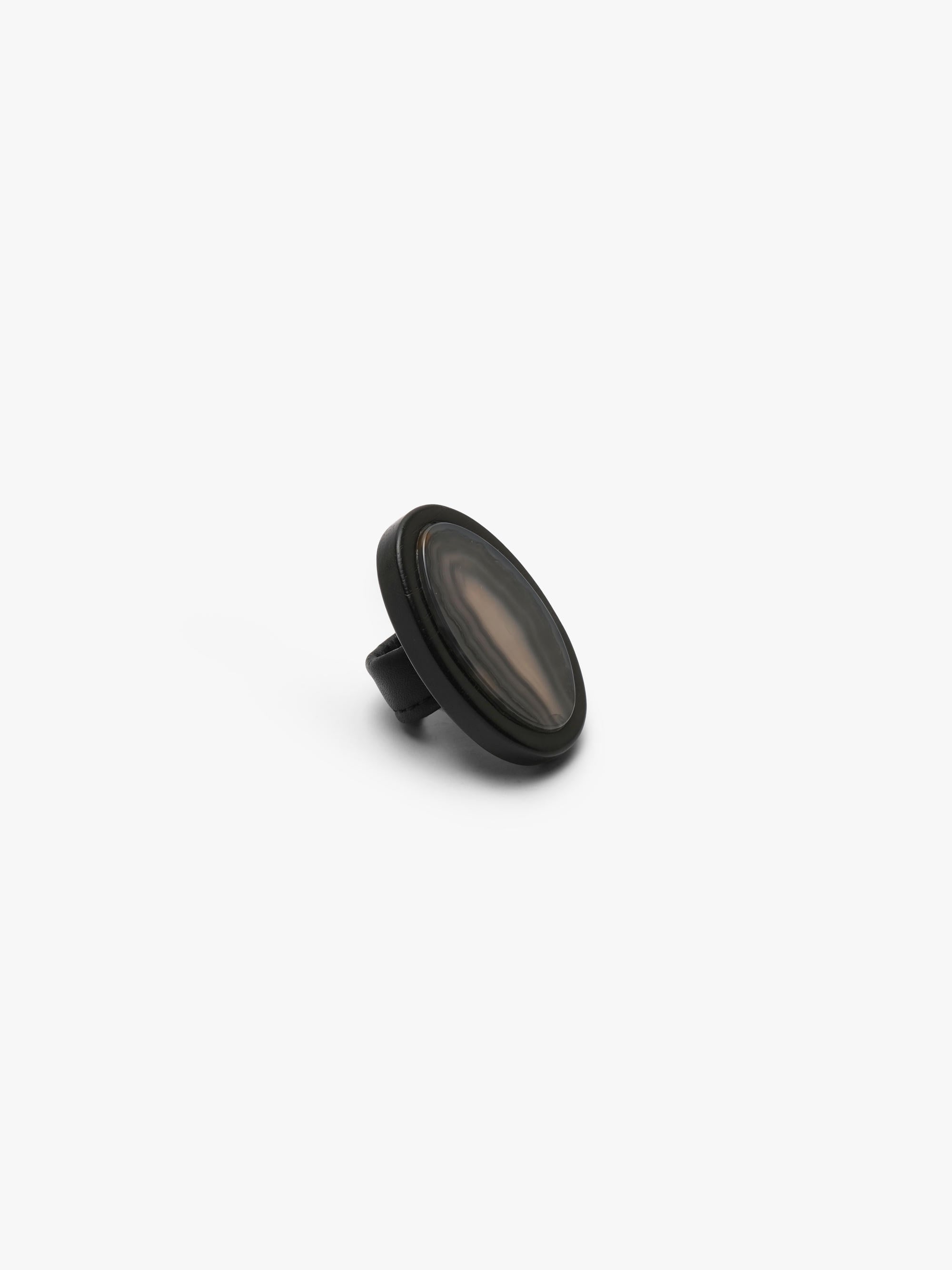 A ring with a patterened black and brown stone , shown against a solid off-white background.
