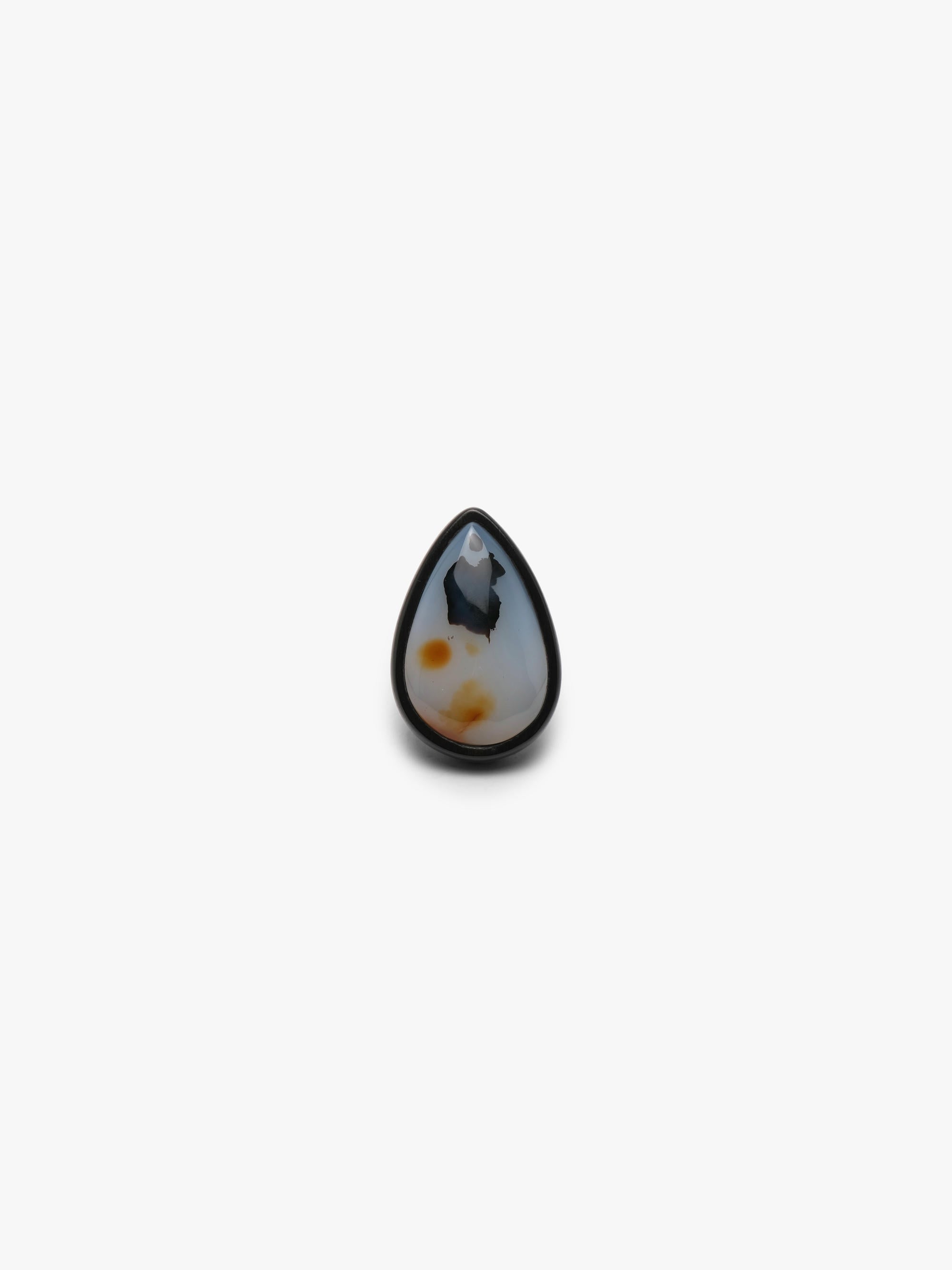 A ring with a white and orange pear-shaped gemstone set into dark wood on a white background