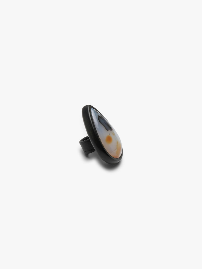 A ring with a white and orange pear-shaped gemstone set into dark wood on a white background
