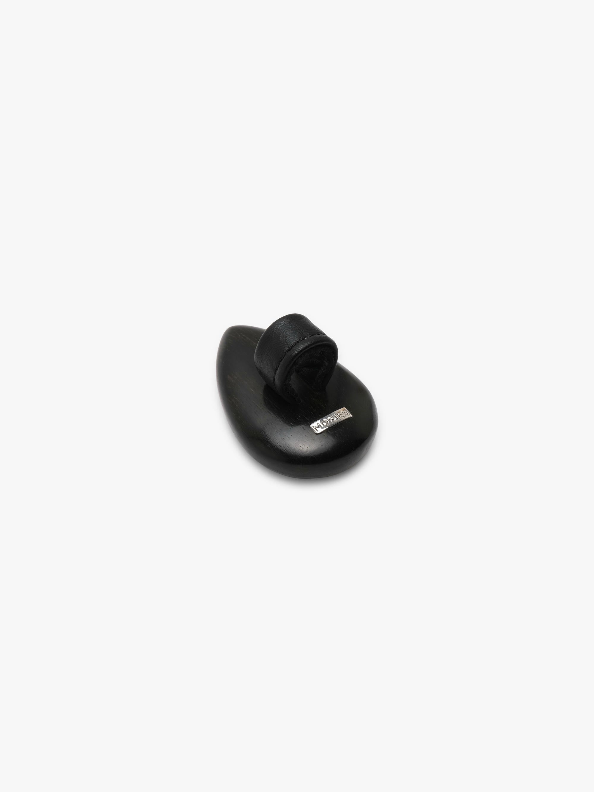 A ring with a white and orange pear-shaped gemstone set into dark wood on a white background