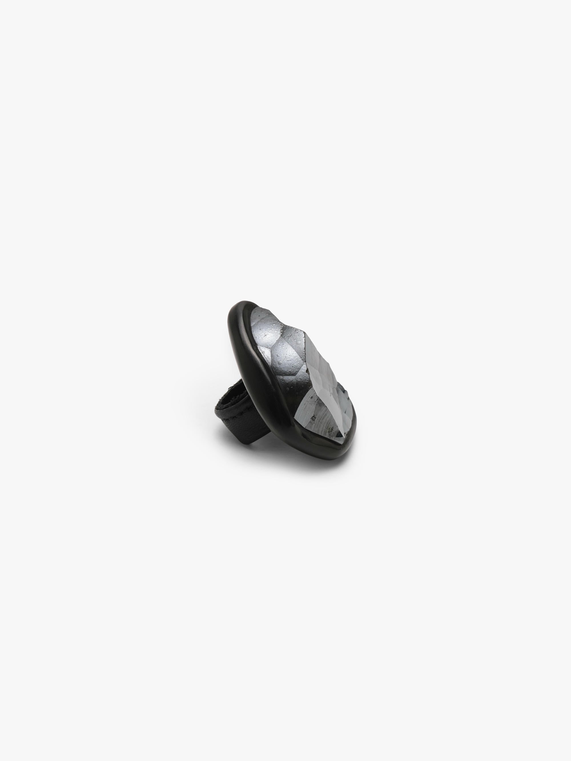 A metallic textured ring with a black stone set into black horn with a leather band, displayed on a white background.