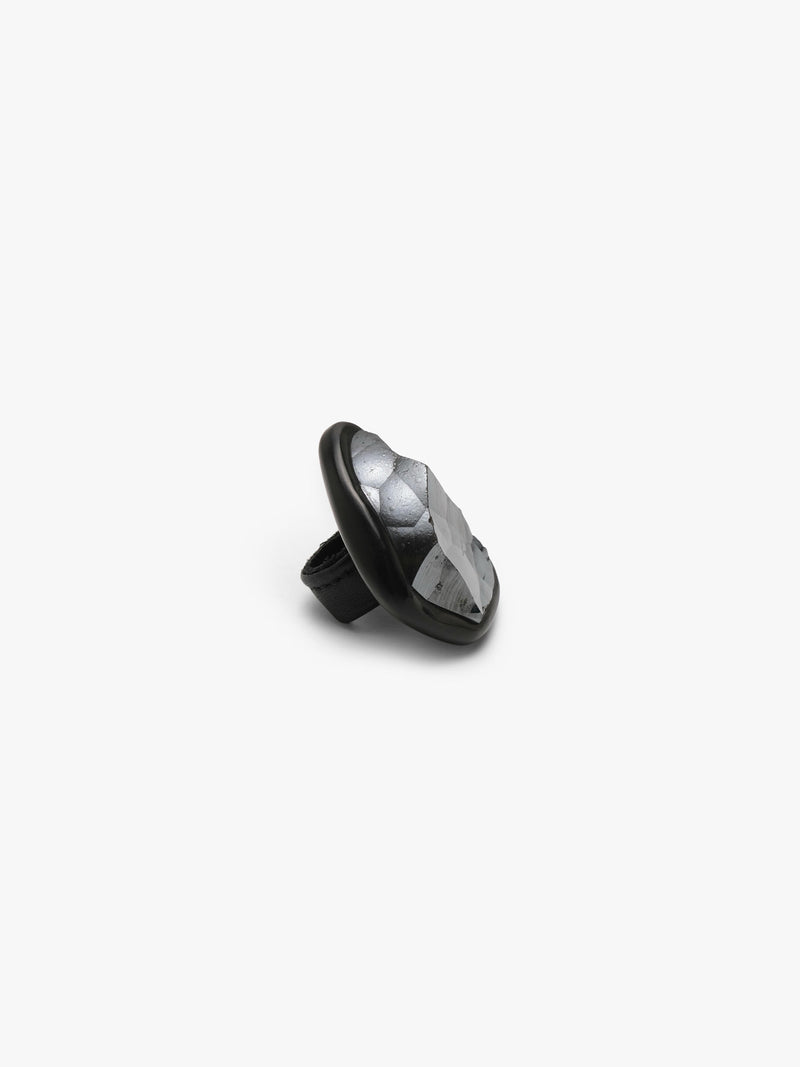 A metallic textured ring with a black stone set into black horn with a leather band, displayed on a white background.