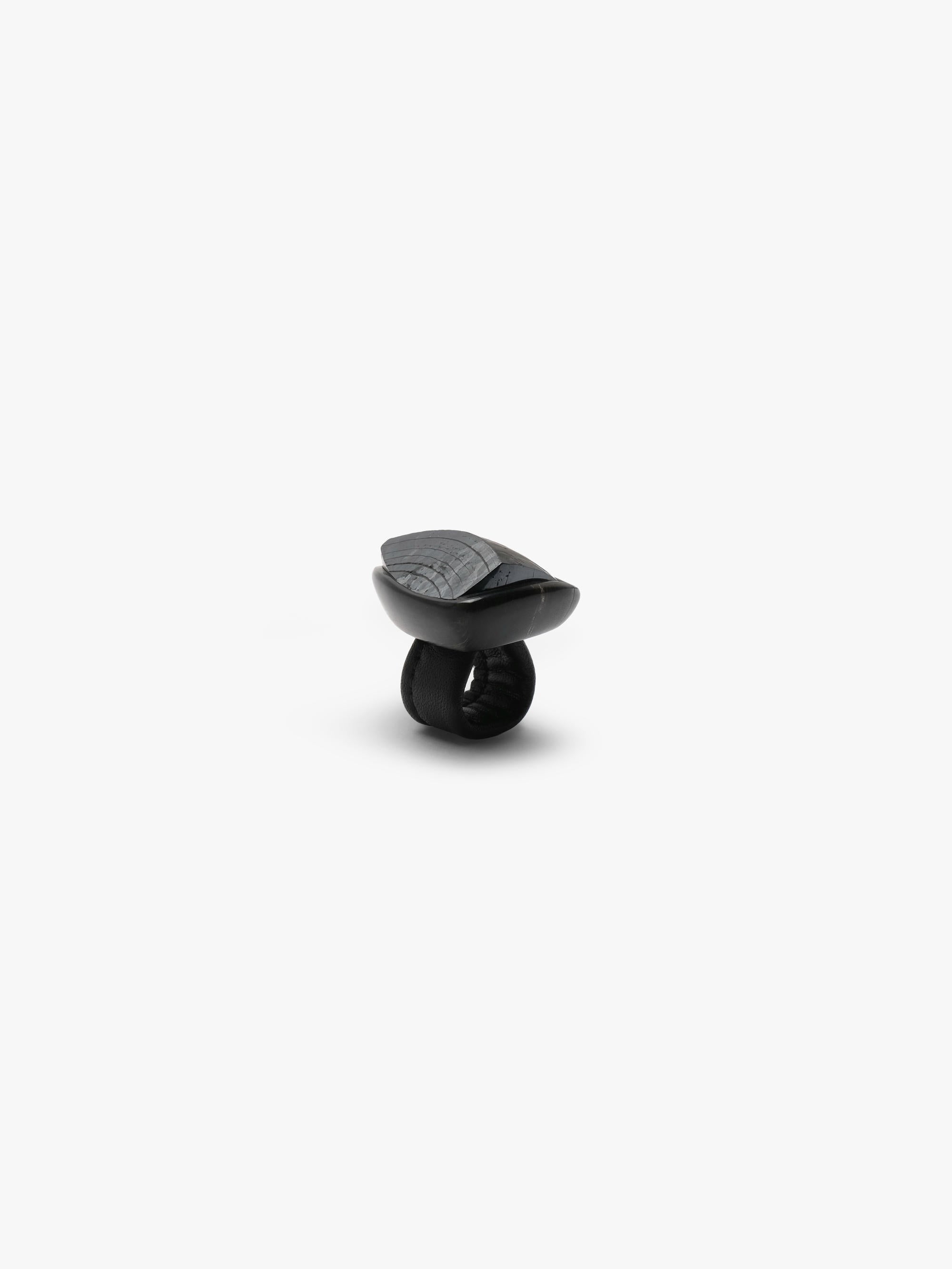 A sculptural black ring featuring a glossy, rounded top section and a thick, matte black band, photographed against a solid light gray background.