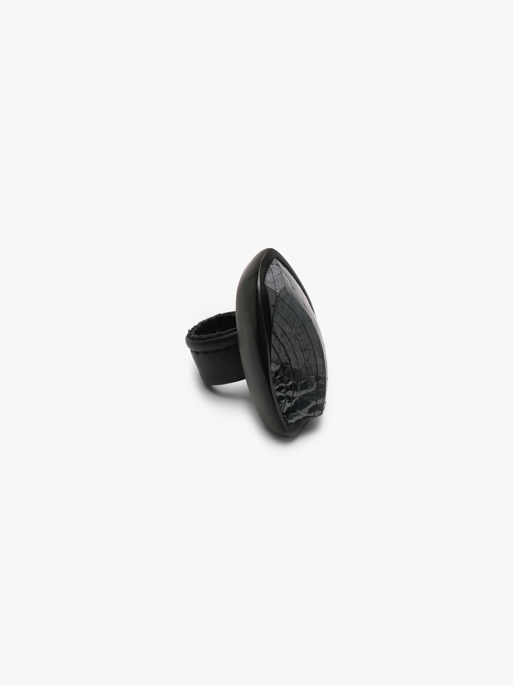A sculptural black ring featuring a glossy, rounded top section and a thick, matte black band, photographed against a solid light gray background.
