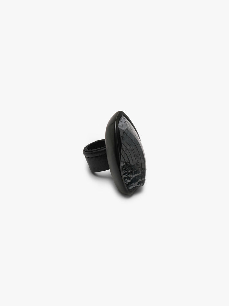 A sculptural black ring featuring a glossy, rounded top section and a thick, matte black band, photographed against a solid light gray background.