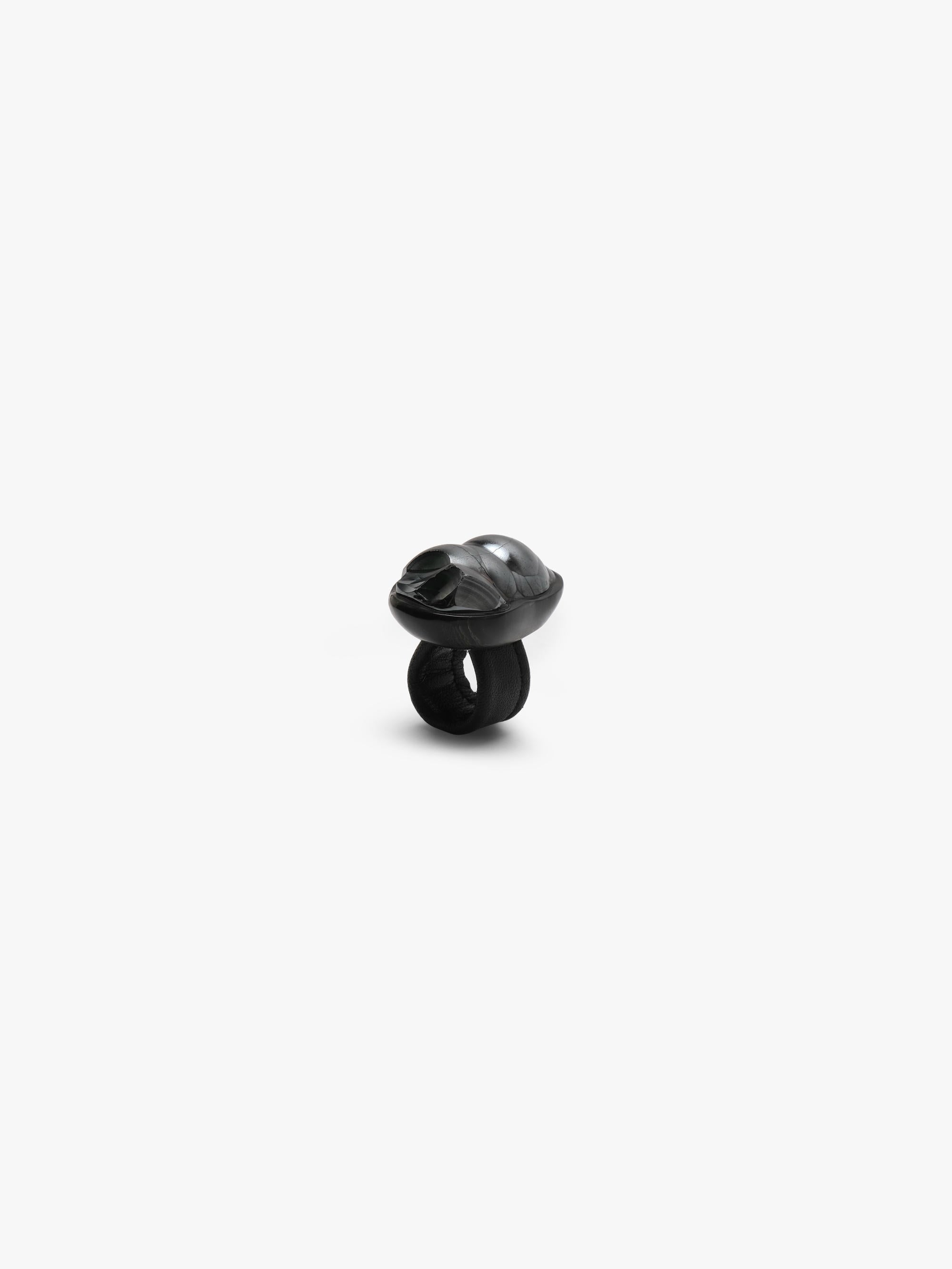 A metallic textured ring with a black stone set into black horn with a leather band, displayed on a white background.