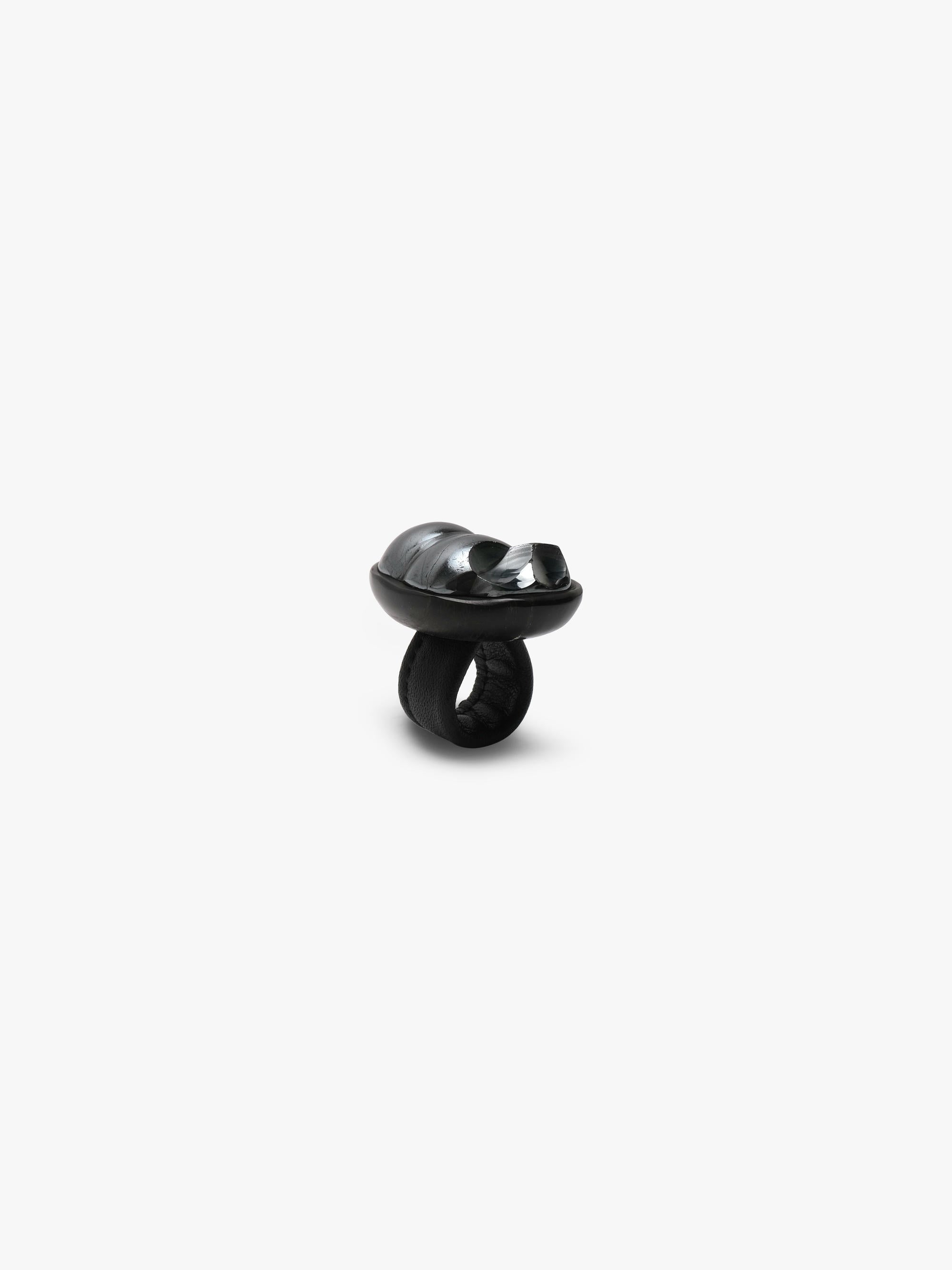 A black sculptural metallic textured ring with a black stone set into black horn with a leather band, displayed on a white background.