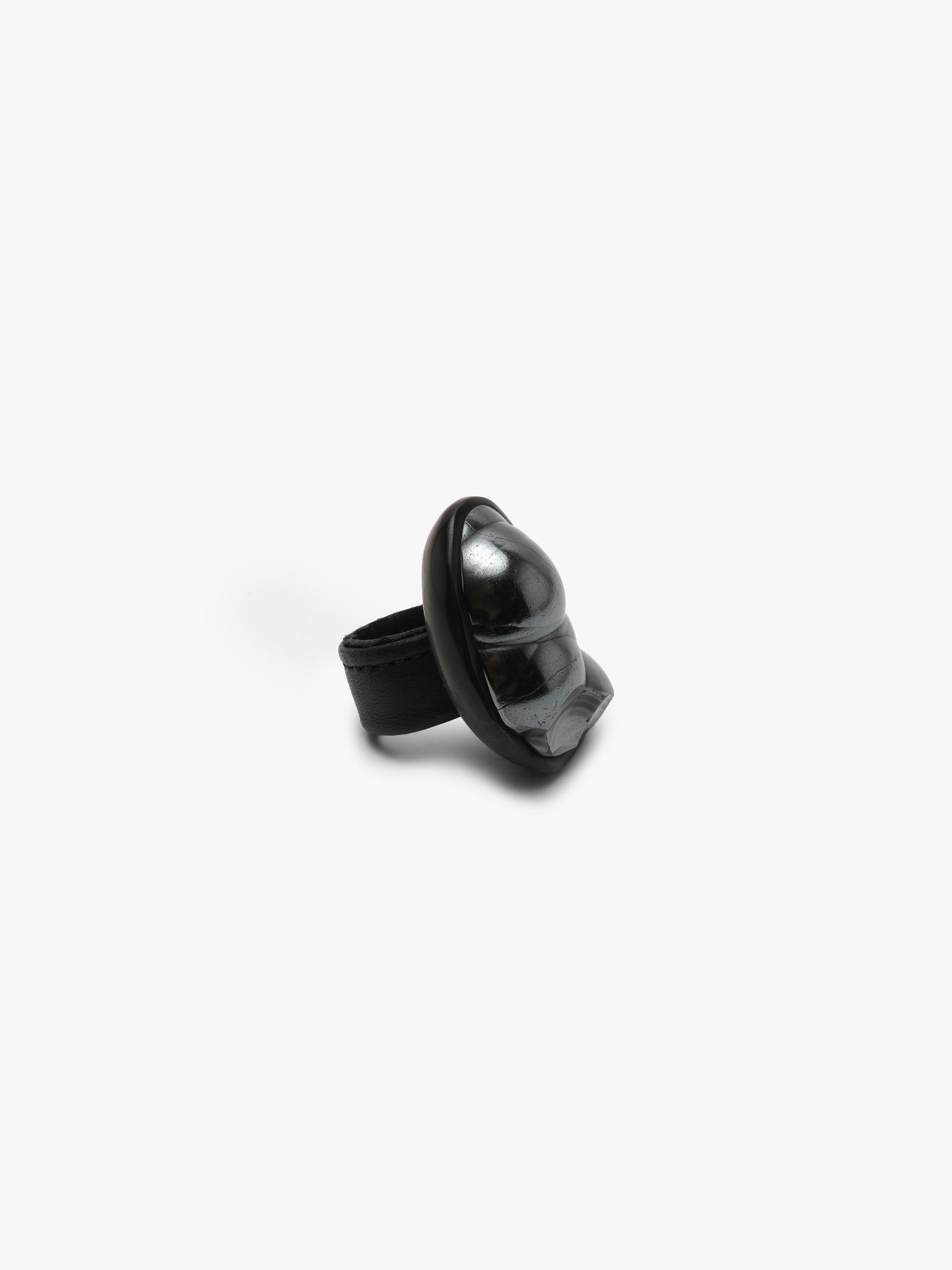 A black sculptural metallic textured ring with a black stone set into black horn with a leather band, displayed on a white background.