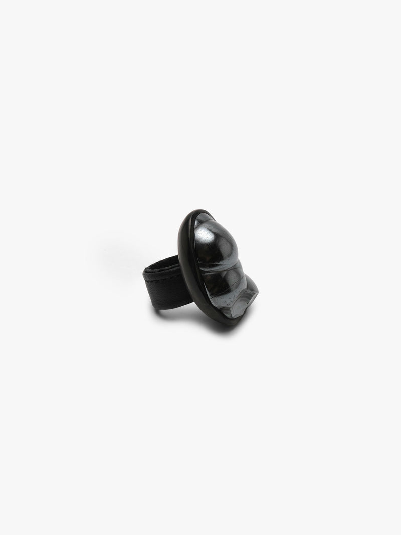 A black sculptural metallic textured ring with a black stone set into black horn with a leather band, displayed on a white background.