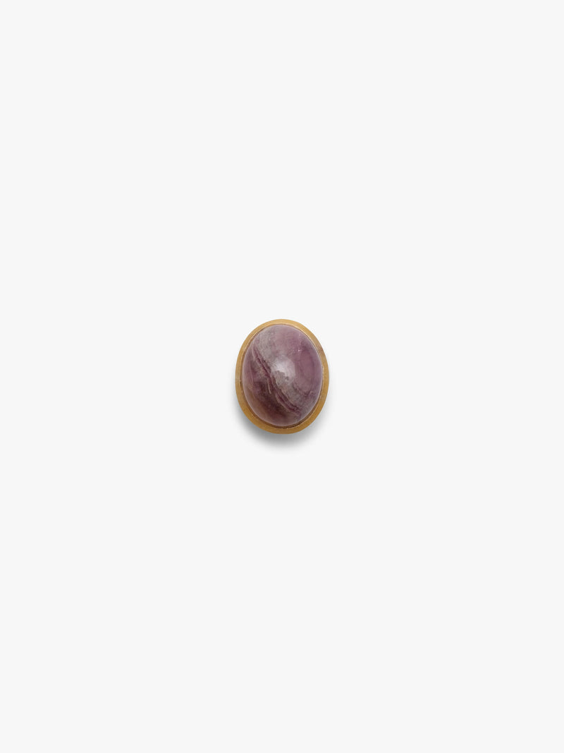 An oval cabochon gemstone with a purple and pink marbled pattern, set in a gold colored bezel, centered on a plain white background.