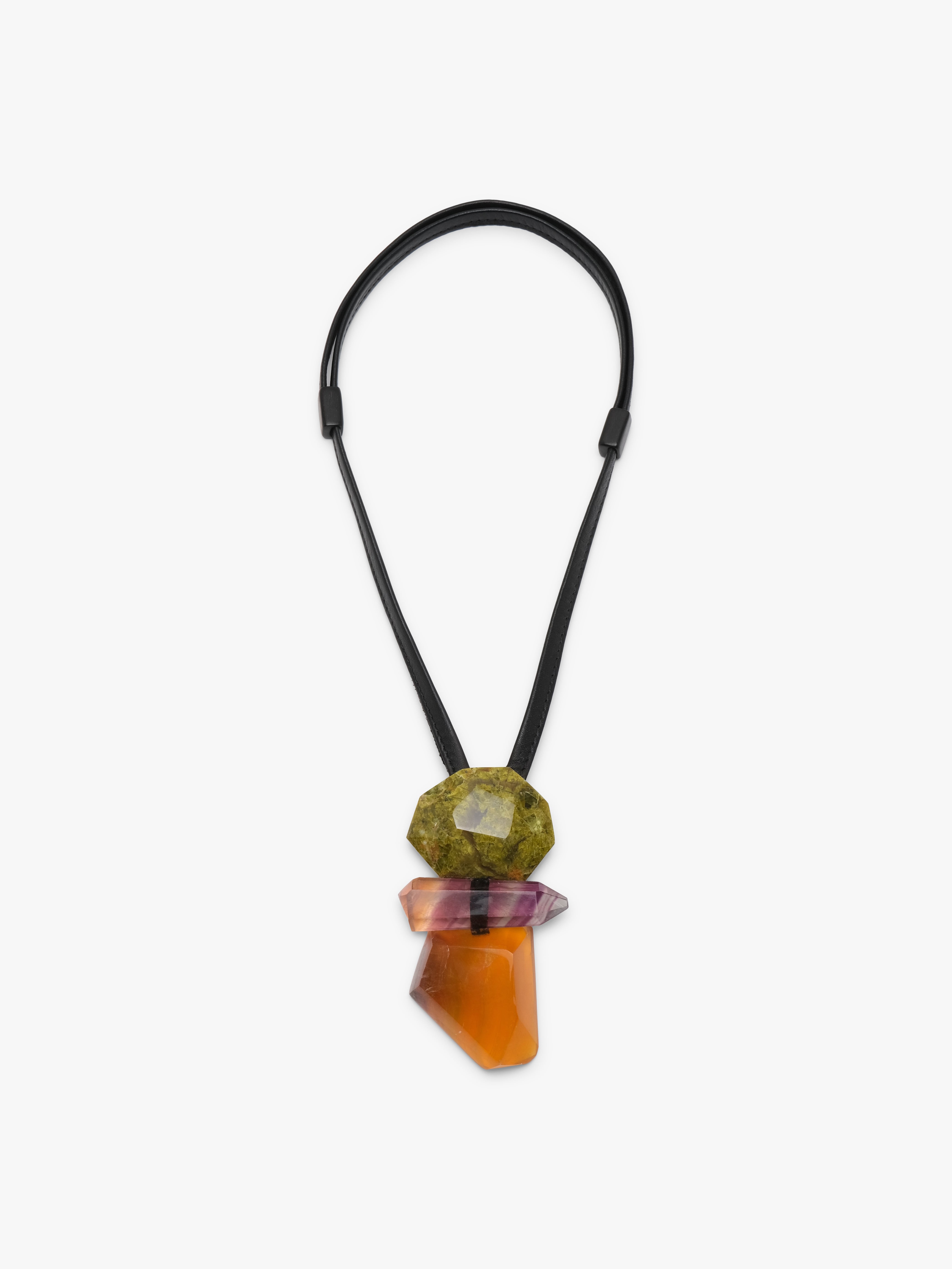 A black cord necklace featuring a stacked crystal pendant with a green stone on top, a pinkish-purple stone in the middle, and a faceted orange stone at the bottom, shown against a plain light gray background.