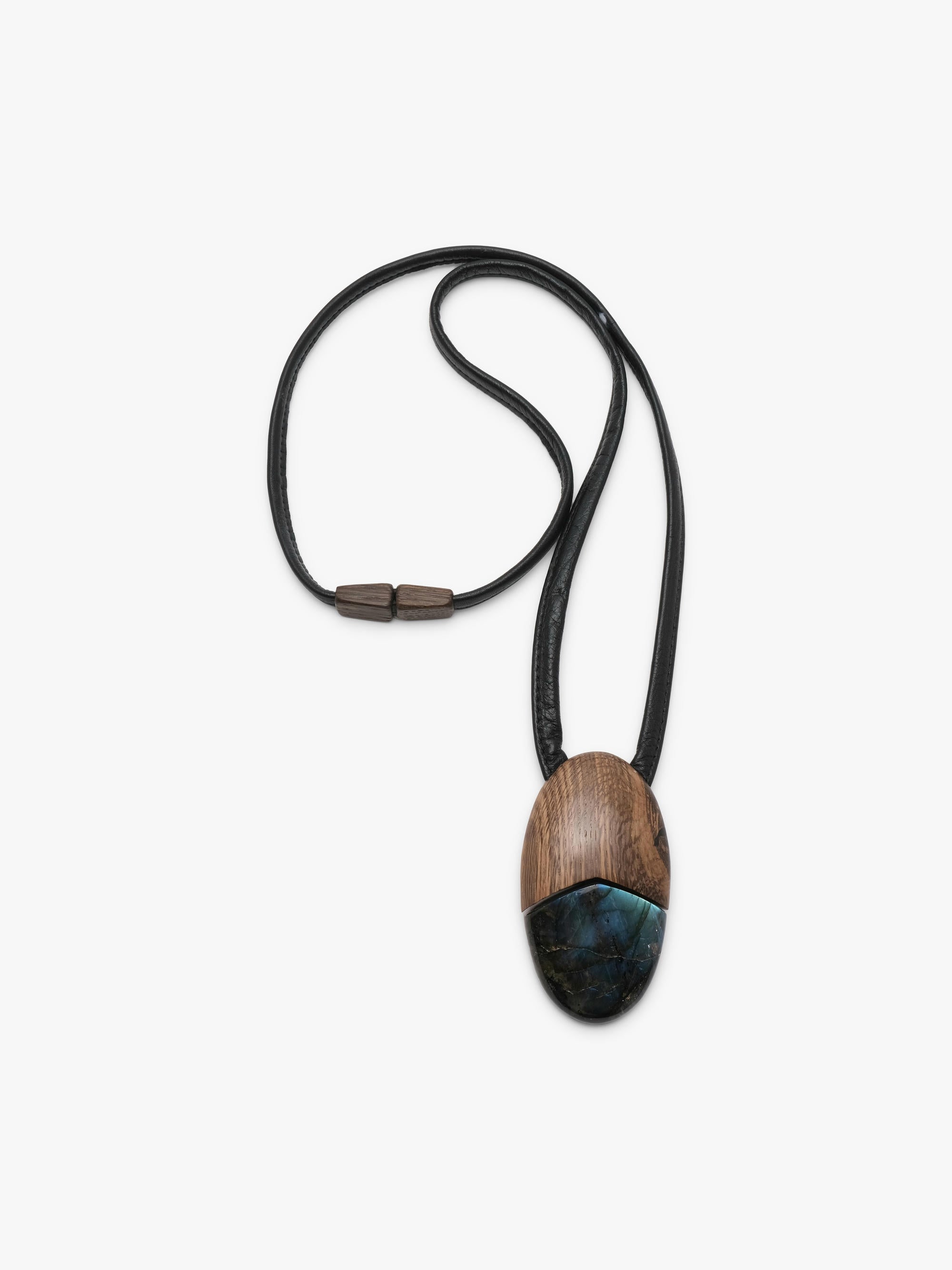 A wooden pendant necklace featuring a split design with a warm brown wood grain top half and a dark blue-green stone bottom half, suspended on a black cord with a silver-toned clasp, set against a plain light gray background.