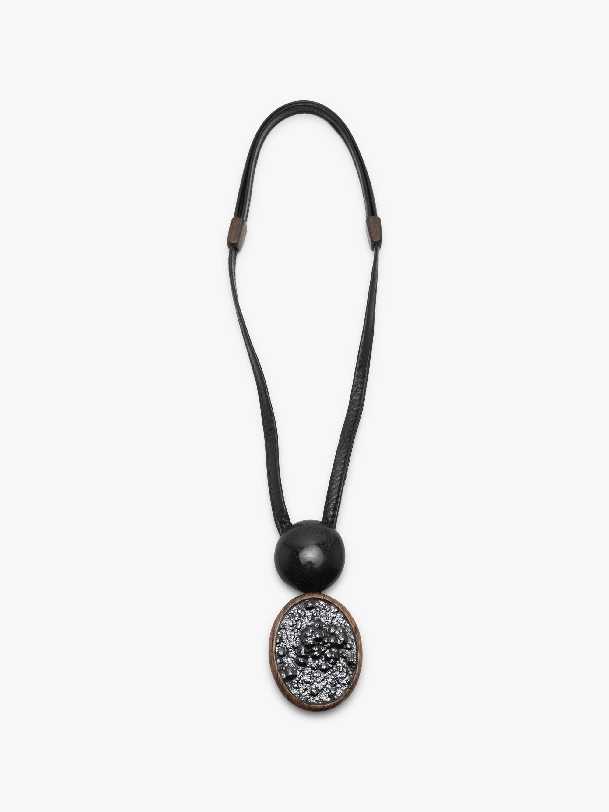 A black leather cord necklace featuring a large round black bead and an oval pendant with a textured black pattern surrounded by a bronze-toned border, shown against a plain white background.