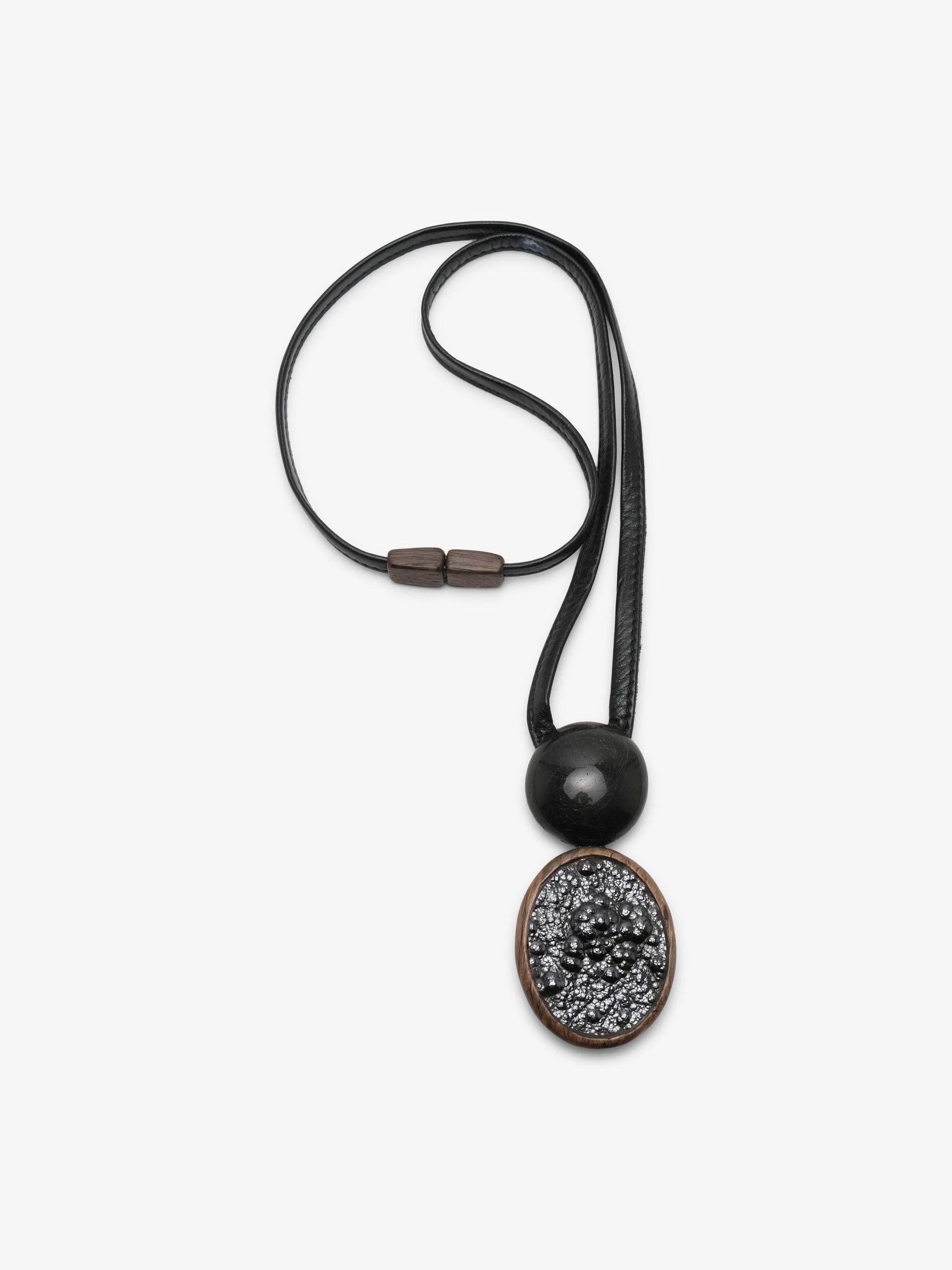 A black leather cord necklace featuring a round black bead and a textured oval pendant with a bronze-toned border and black-and-white speckled center, shown on a light gray background.