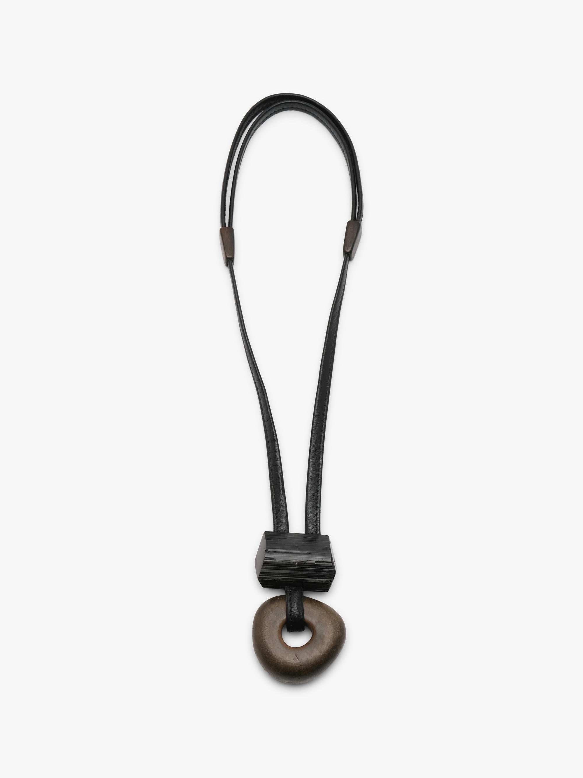 A minimalist black leather cord necklace with a dark brown wooden pendant, displayed vertically against a clean white background.