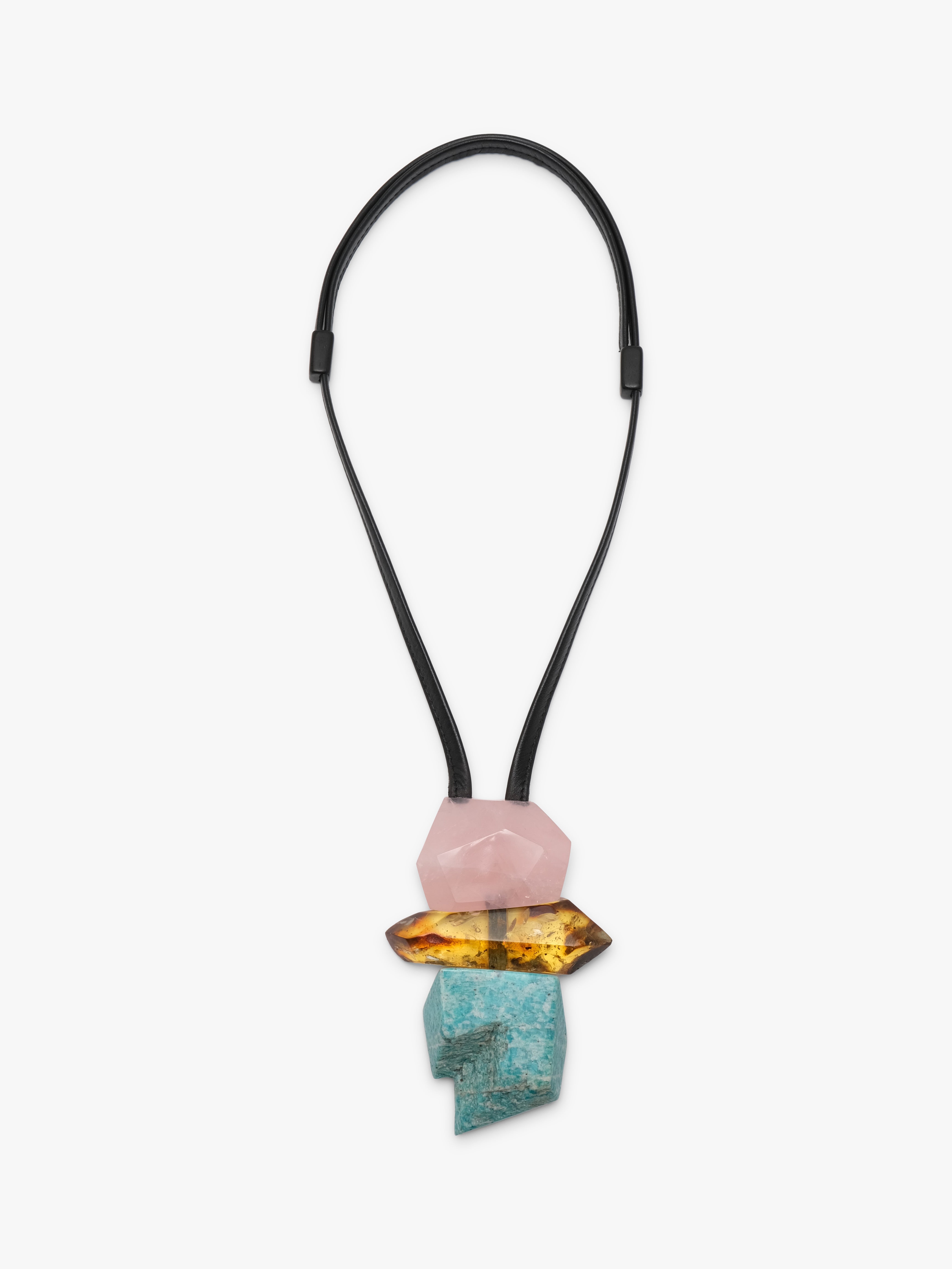 A modern geometric pendant necklace featuring a black elastic cord and a stacked crystal pendant with a pink stone, a yellow-orange stone, and a turquoise stone on a light gray background.