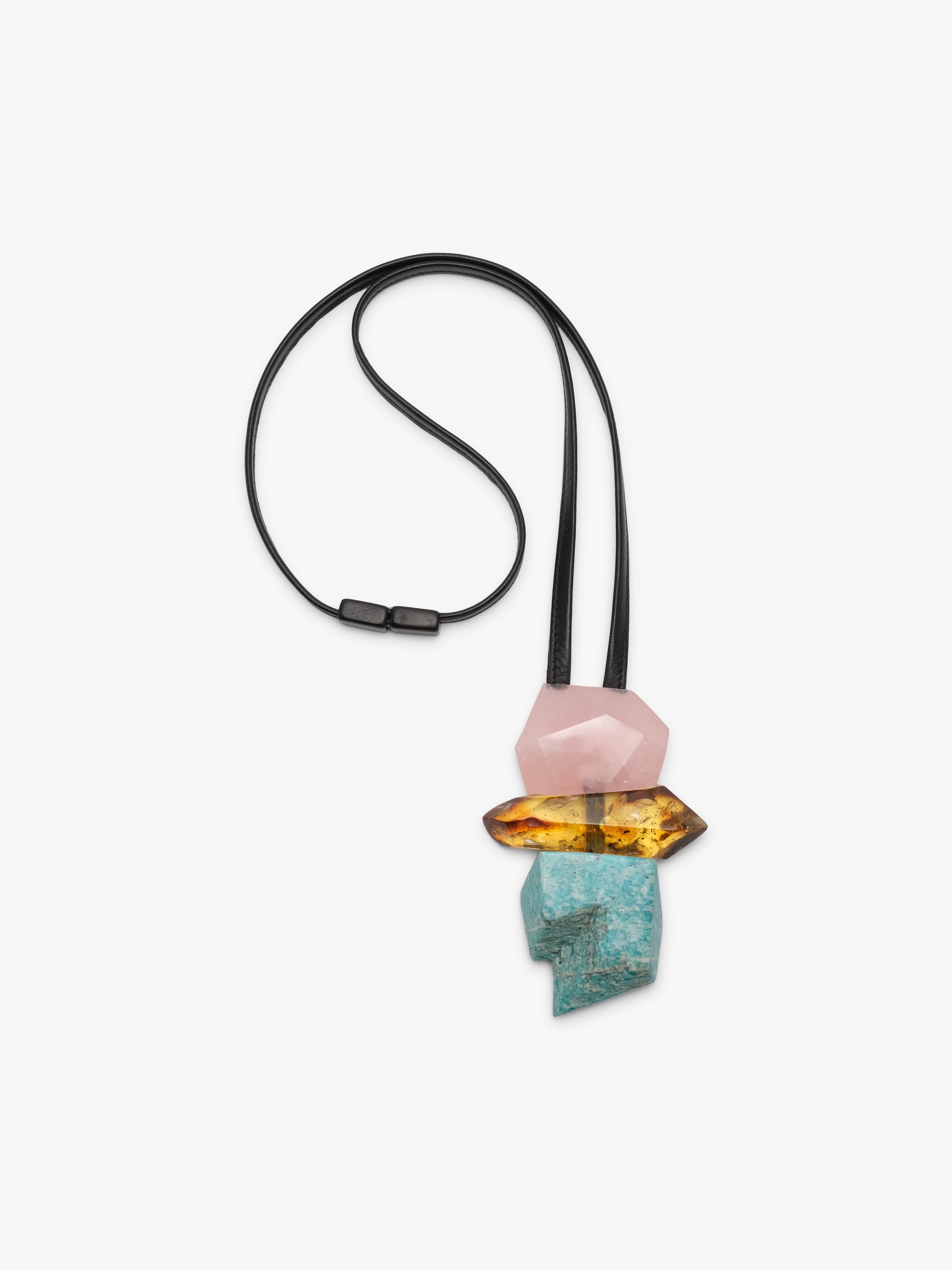 A modern geometric pendant necklace featuring a black elastic cord and a stacked crystal pendant with a pink stone, a yellow-orange stone, and a turquoise stone on a light gray background.