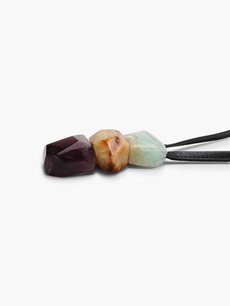 Black leather pendant with a cluster of natural stones in light blue, golden and purple colors. Displayed on a white background.
