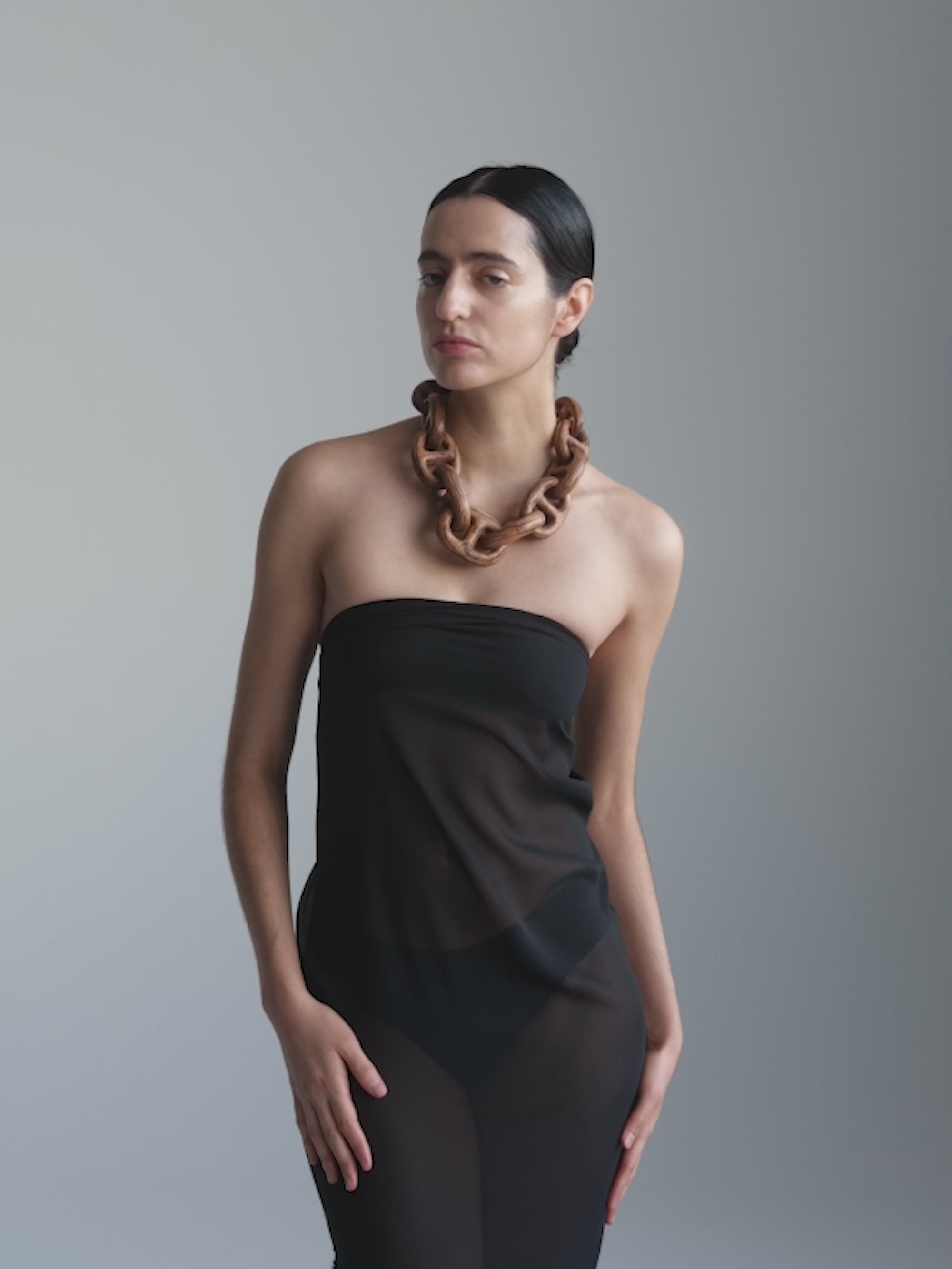 Woman wearing a large, wooden necklace against a plain background